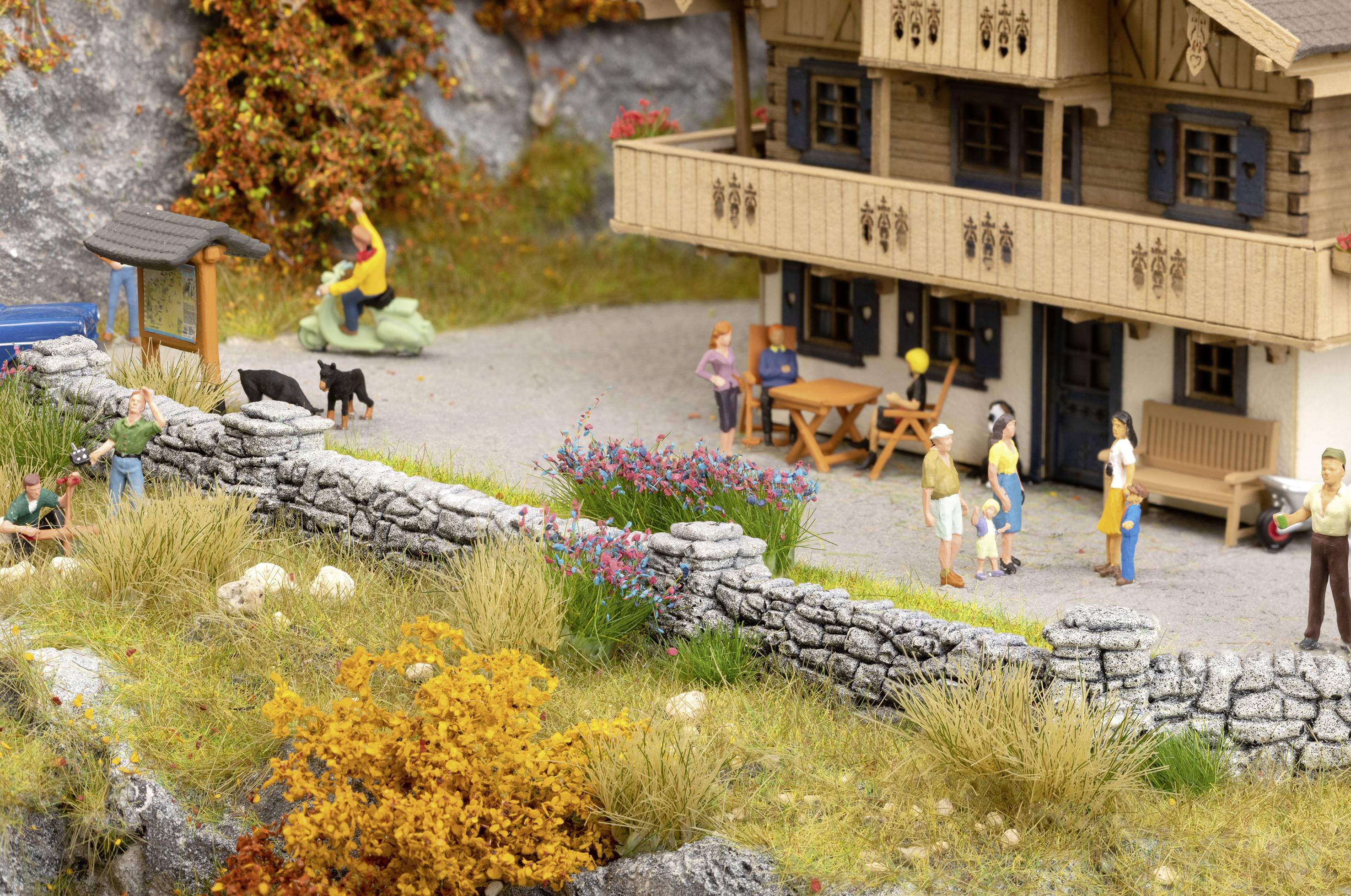 A model of a rural house with people standing outside. Two black dogs are in the yard, surrounded by an autumnal landscape.