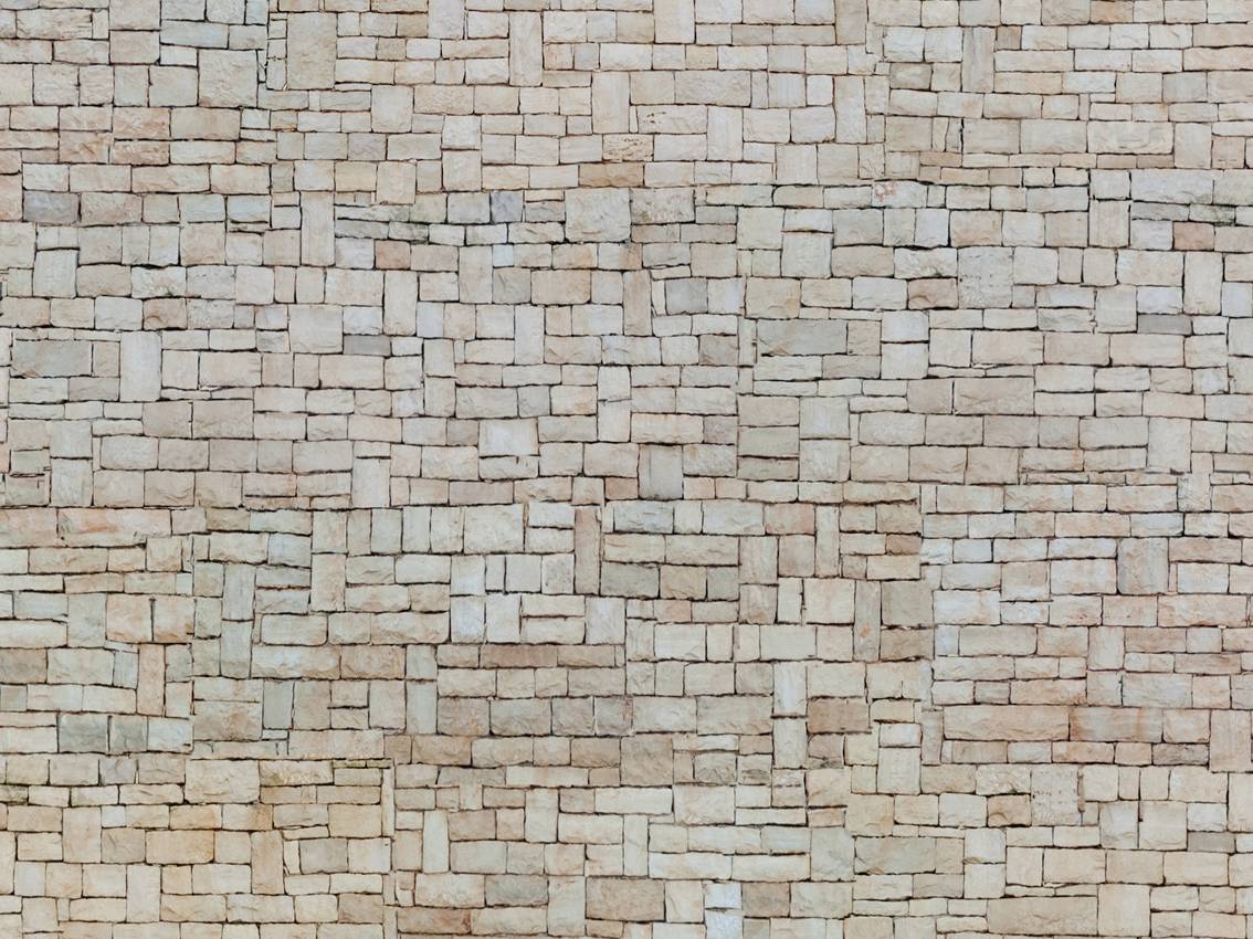 Brick wall with an irregular pattern, consisting of multi-coloured rectangular bricks in beige and brown shades.