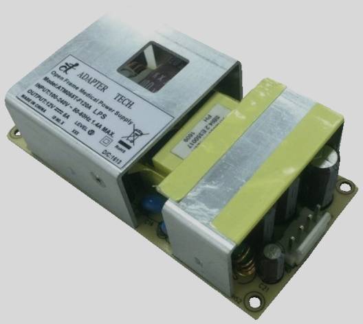 An open power supply module with electronic components and a label on top. The label displays technical specifications of the power supply.