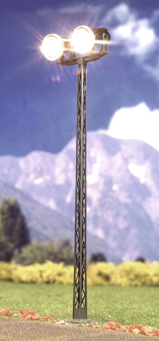 A tall street lamp with two bright lights stands before a mountainous backdrop. Bright clouds and trees in the background.