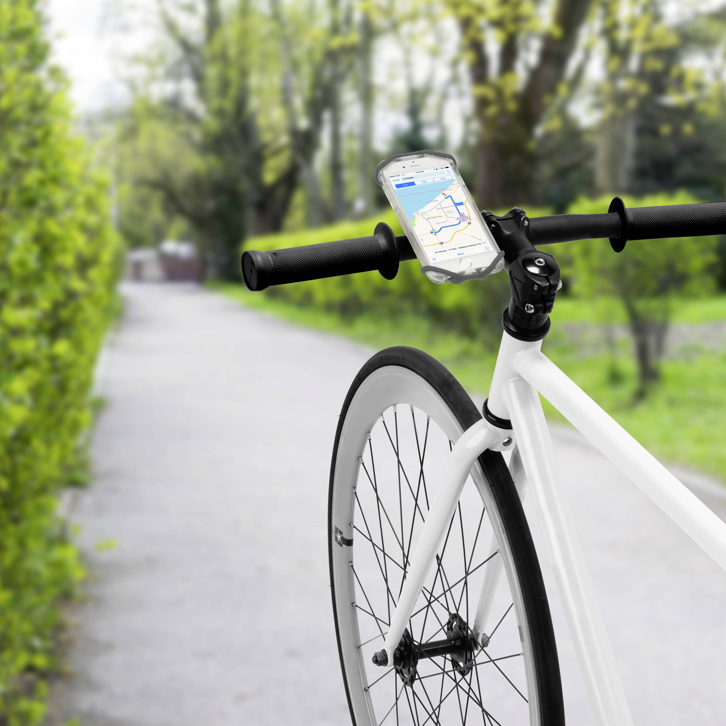 A bicycle is standing on a forest path, its handlebars equipped with a smartphone displaying an open navigation app.
