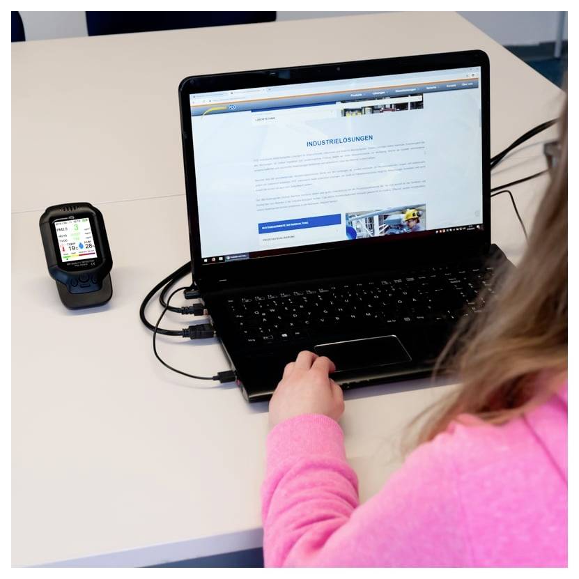 Person using a laptop connected to a handheld device on a desk, with the laptop displaying a German 'Industrielösungen' webpage.