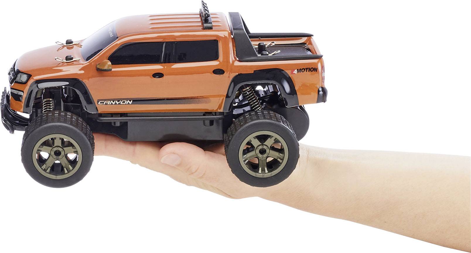 An orange model car in an SUV style is being presented on a hand. It has large wheels and a sporty appearance.