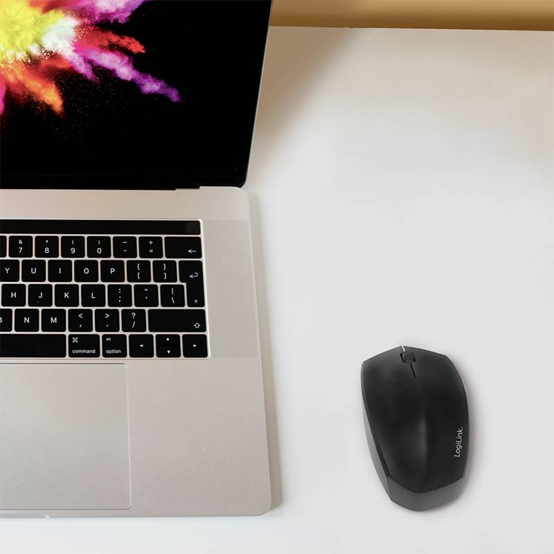 Laptop with a colour explosion on the screen beside a black wireless mouse on a white table.