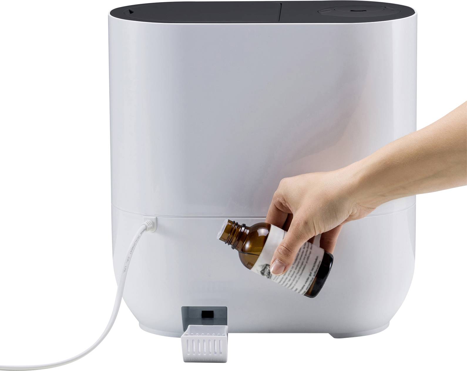A hand is pouring a liquid from a bottle into a white device.