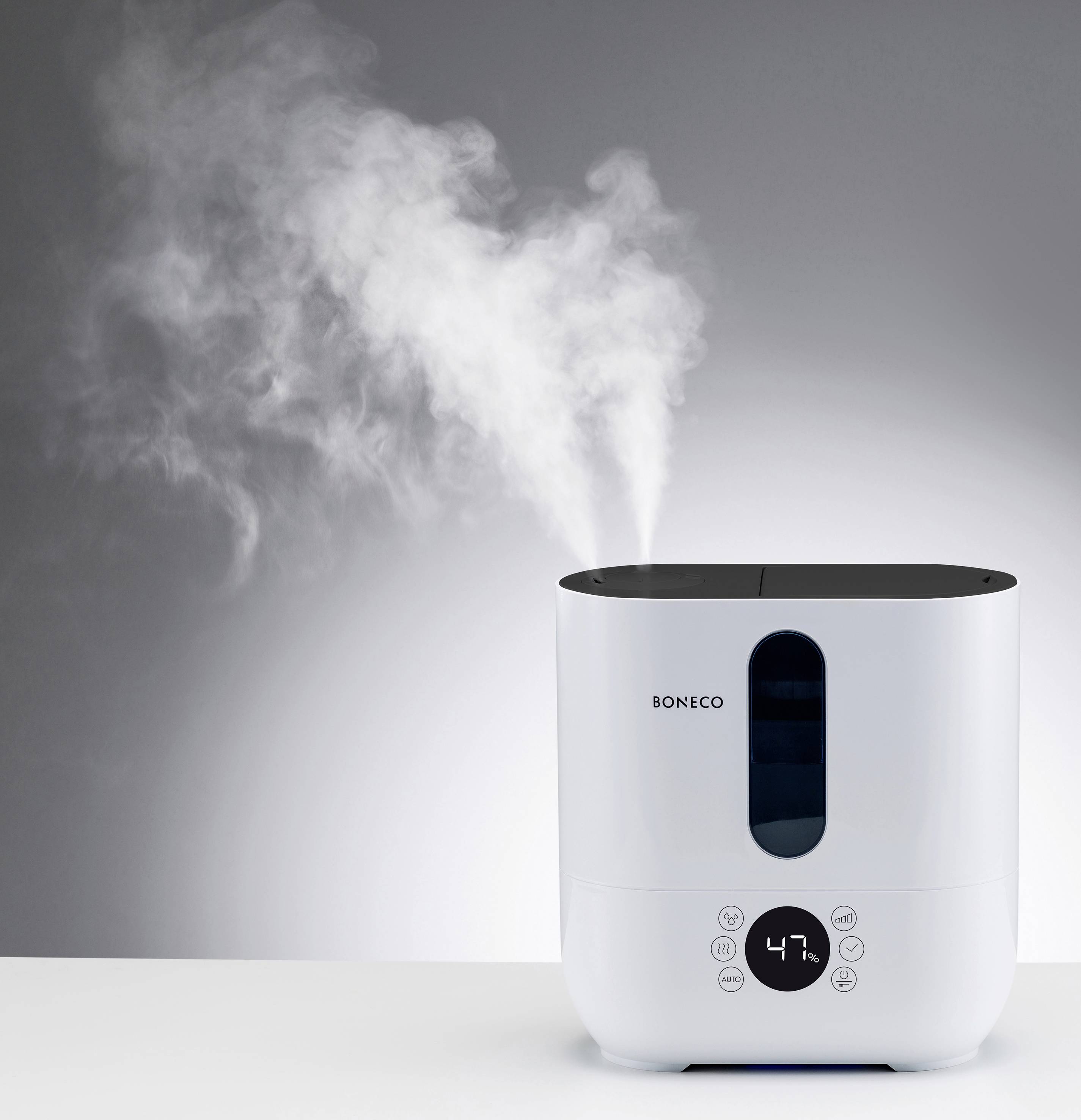 A white air humidifier with a digital display sits on a table, emitting steam. The brand name is 