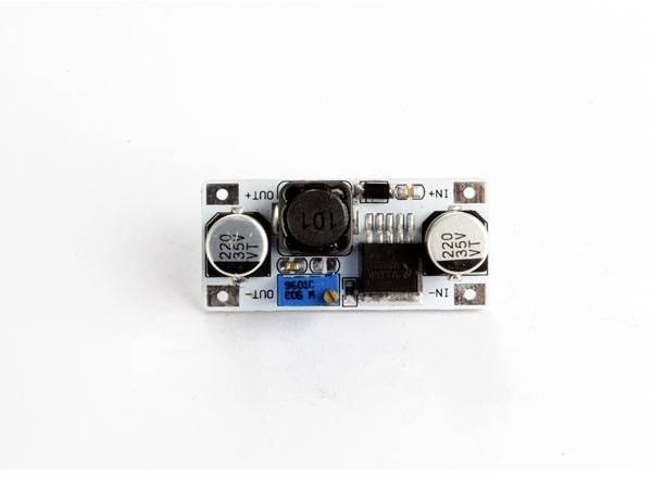 A Spanish voltage regulator module with two capacitors, a core inductor, and terminals labelled 'IN+' and 'OUT-'.