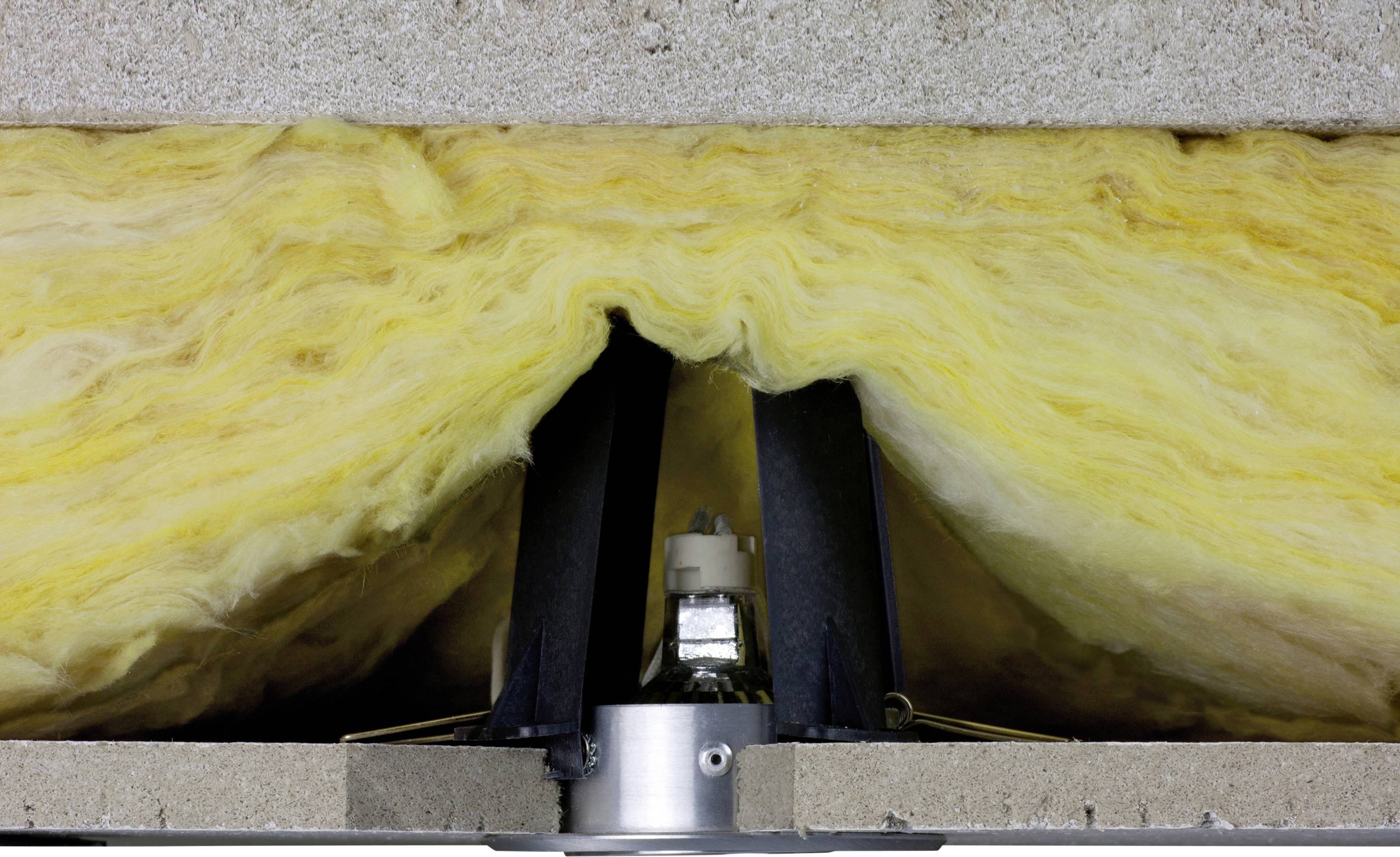 Installation of a ceiling recessed light with yellow insulation. The light is embedded between two layers of building material and surrounded by insulation.