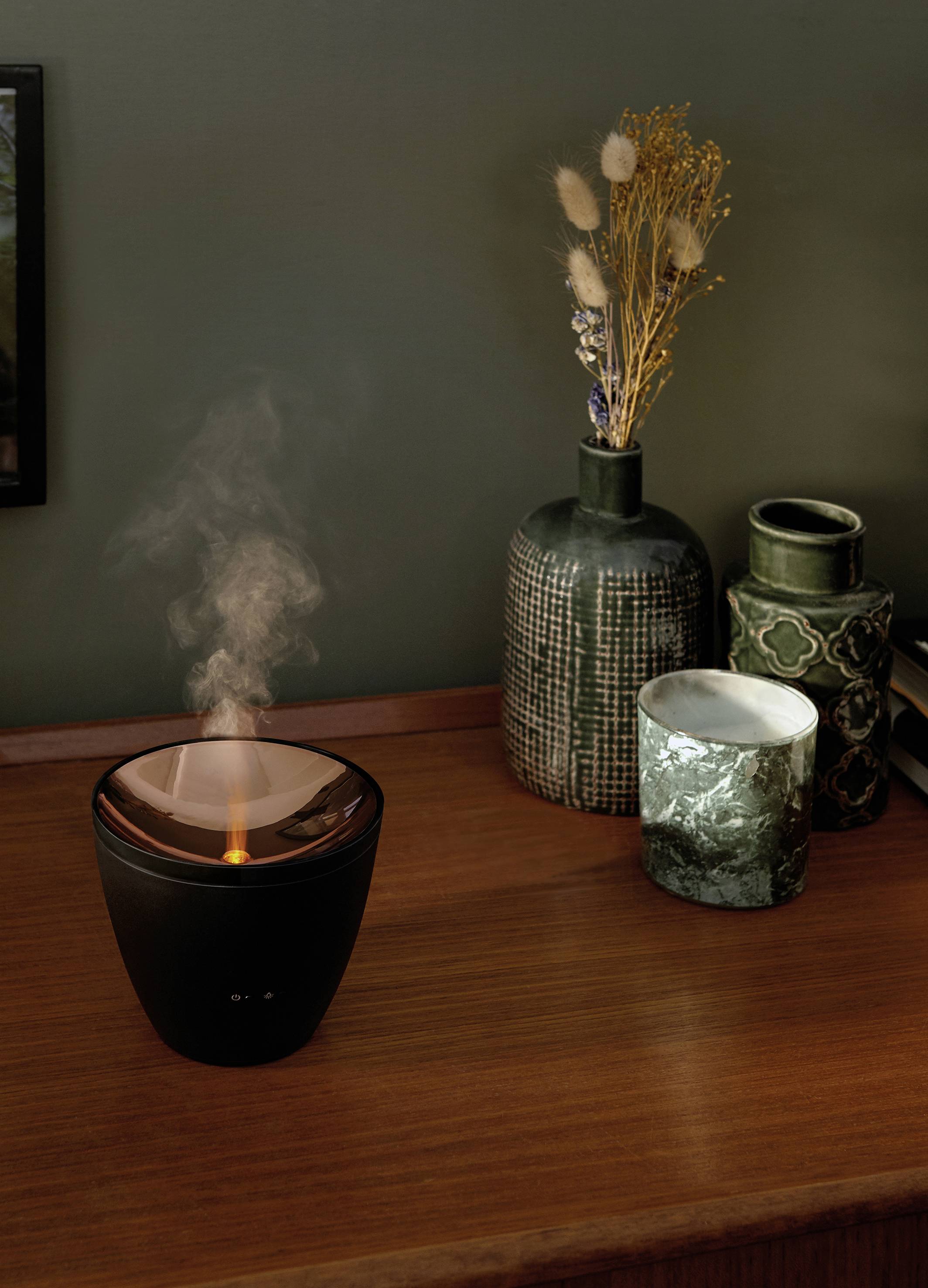 A humidifier on a wooden table, steaming beside decorative vases. The scene conveys a sense of calm and cosiness.