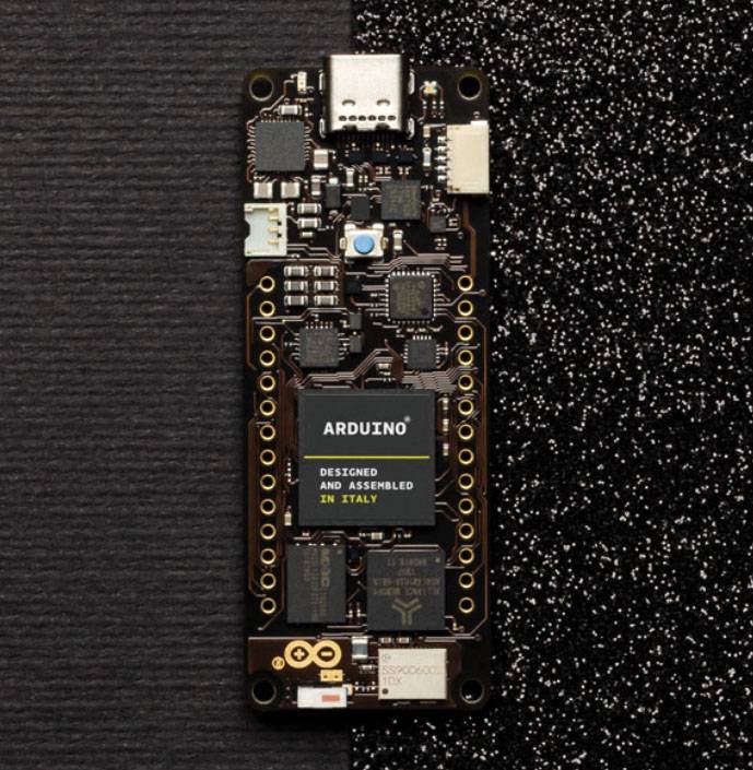 Close-up of a black Arduino board with multiple small electronic components and connectors, on a black surface.