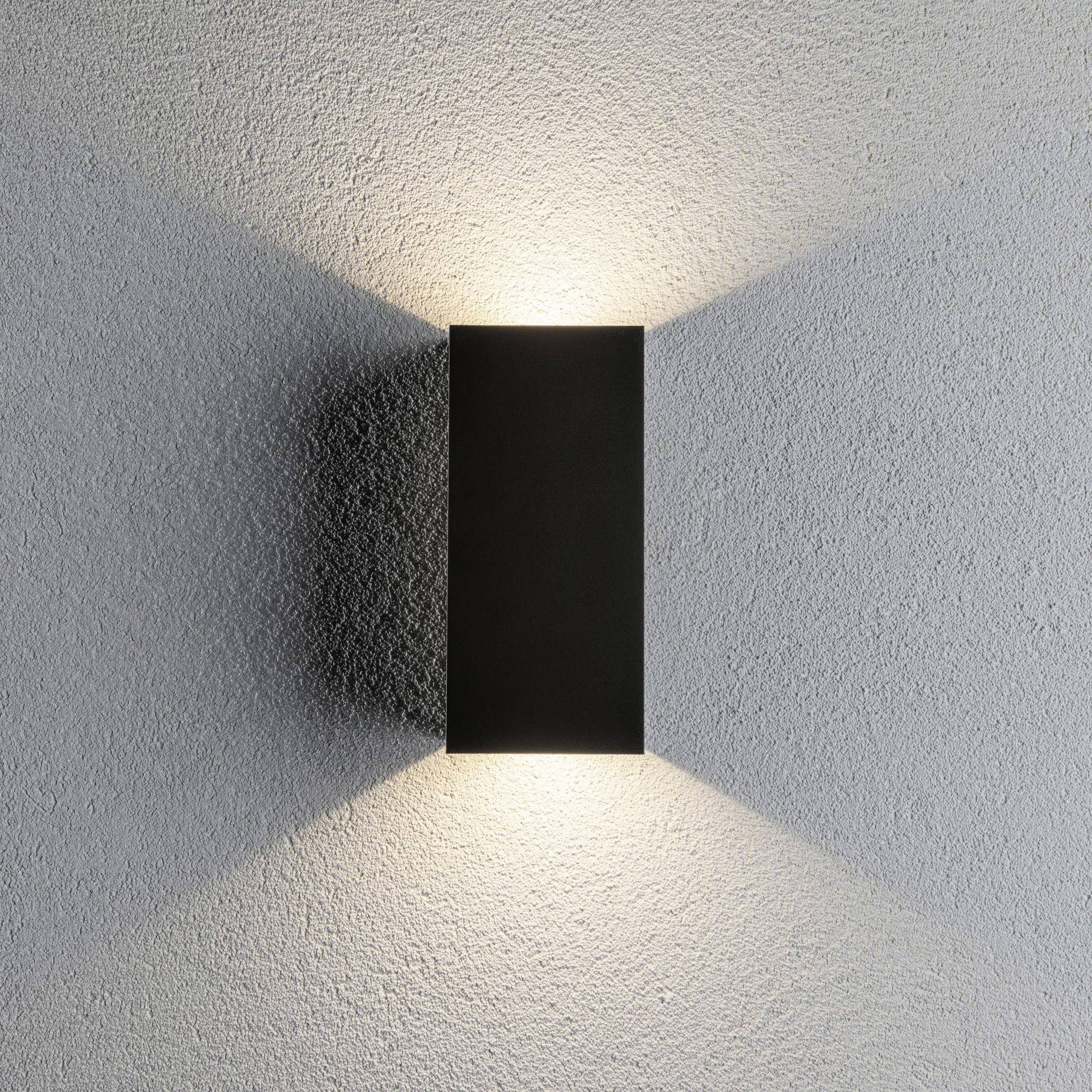 A rectangular, black wall light casts light upwards and downwards onto a grey wall, creating atmospheric light effects.