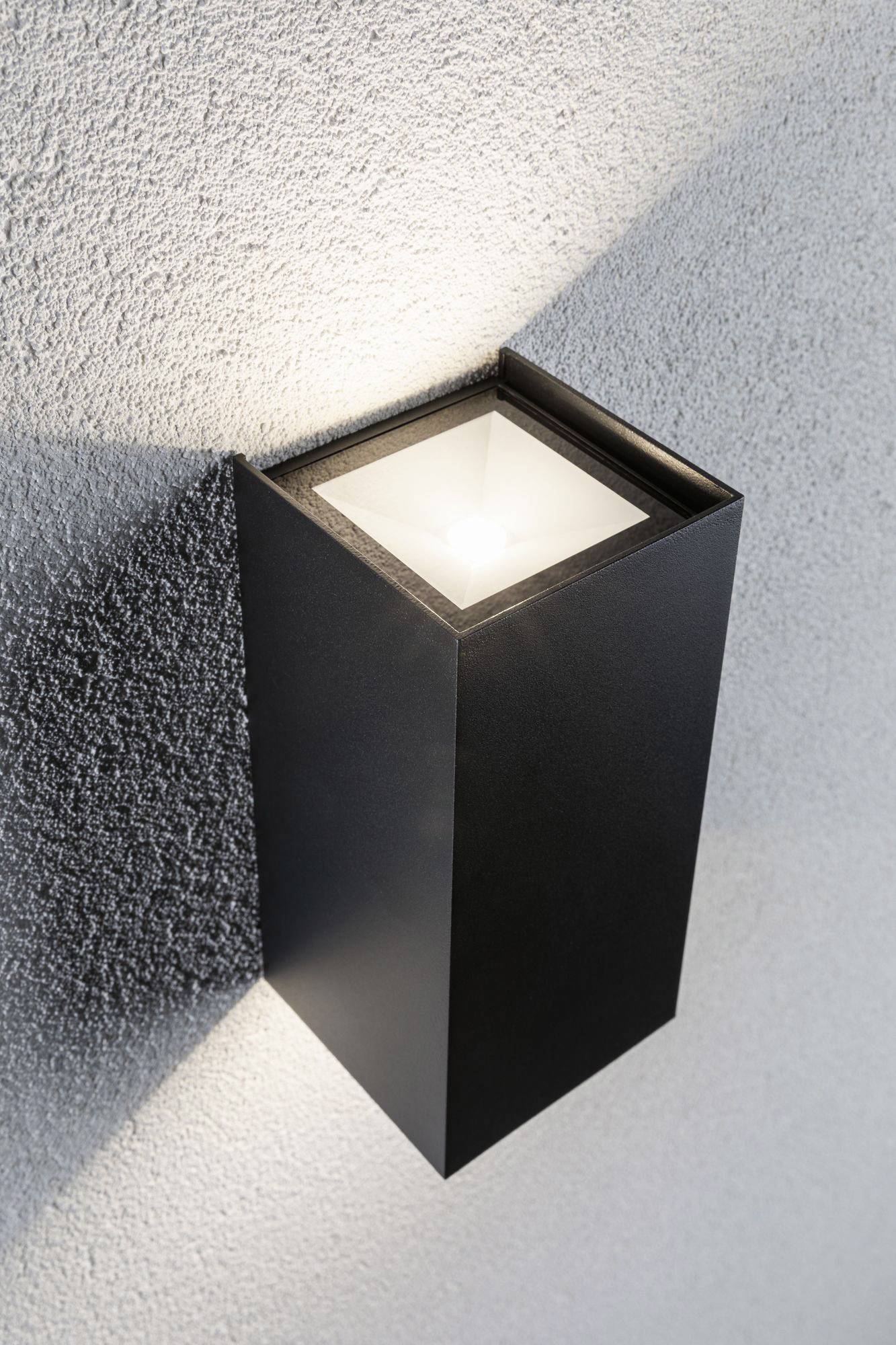 Modern cubic wall light mounted on a textured grey wall. Light radiates upwards and downwards.
