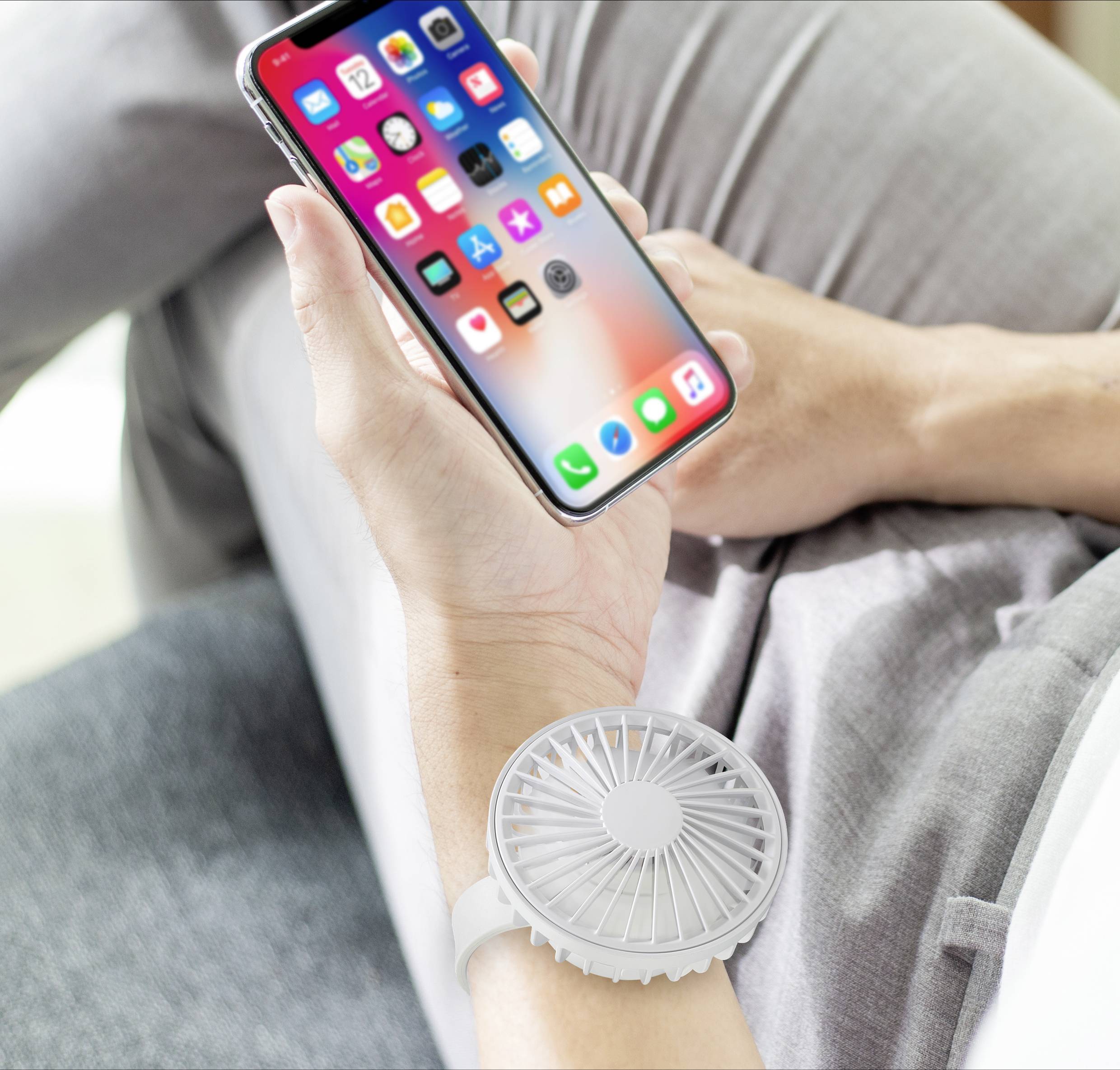 A person is holding a smartphone while a small fan is attached to their wrist.