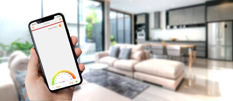 A person is holding a smartphone with an app displaying energy consumption. In the background, a modern living room and kitchen.