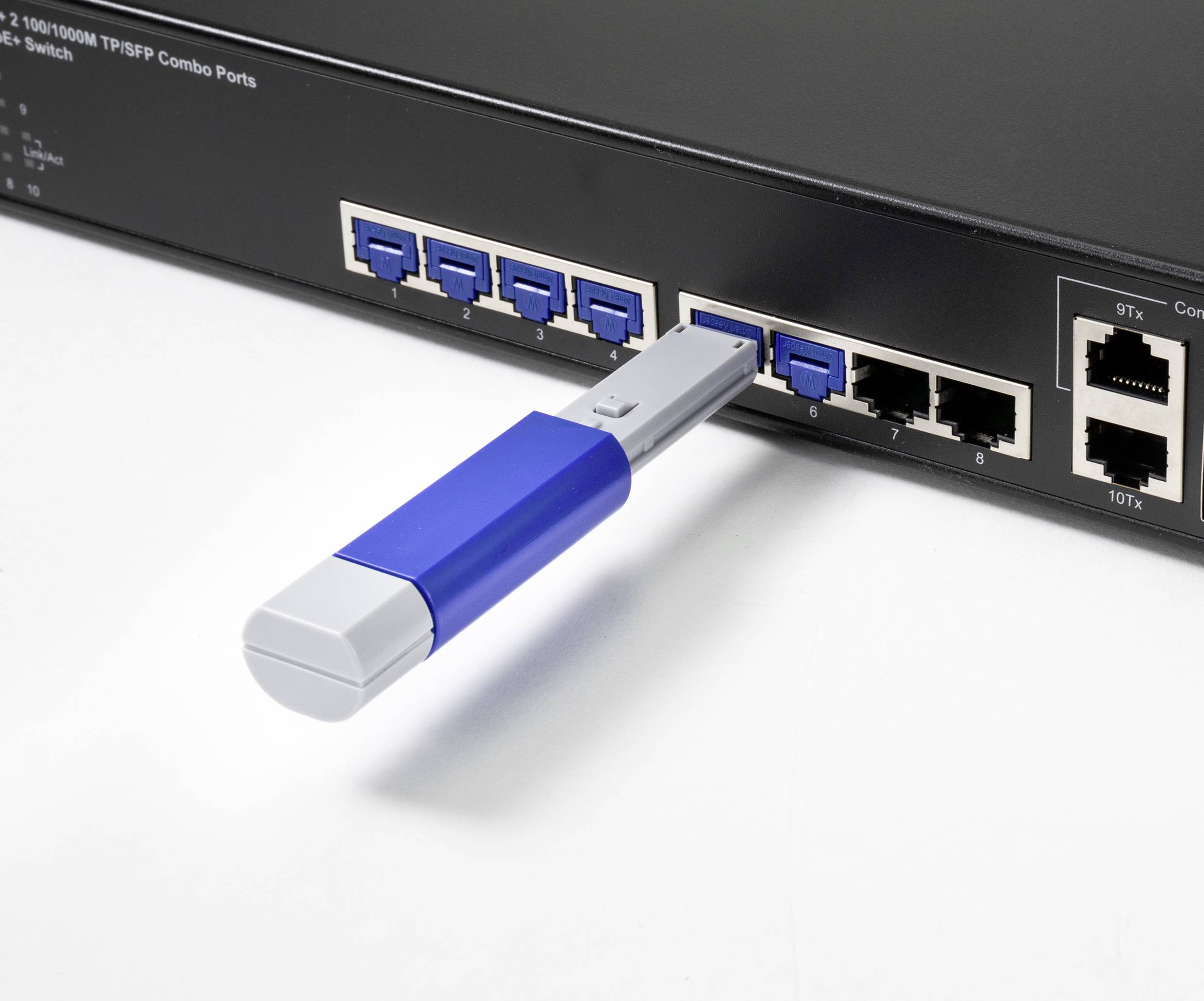 A network switch with a blue-grey USB stick plugged into one of the upper ports. Four ports are visible beside it.
