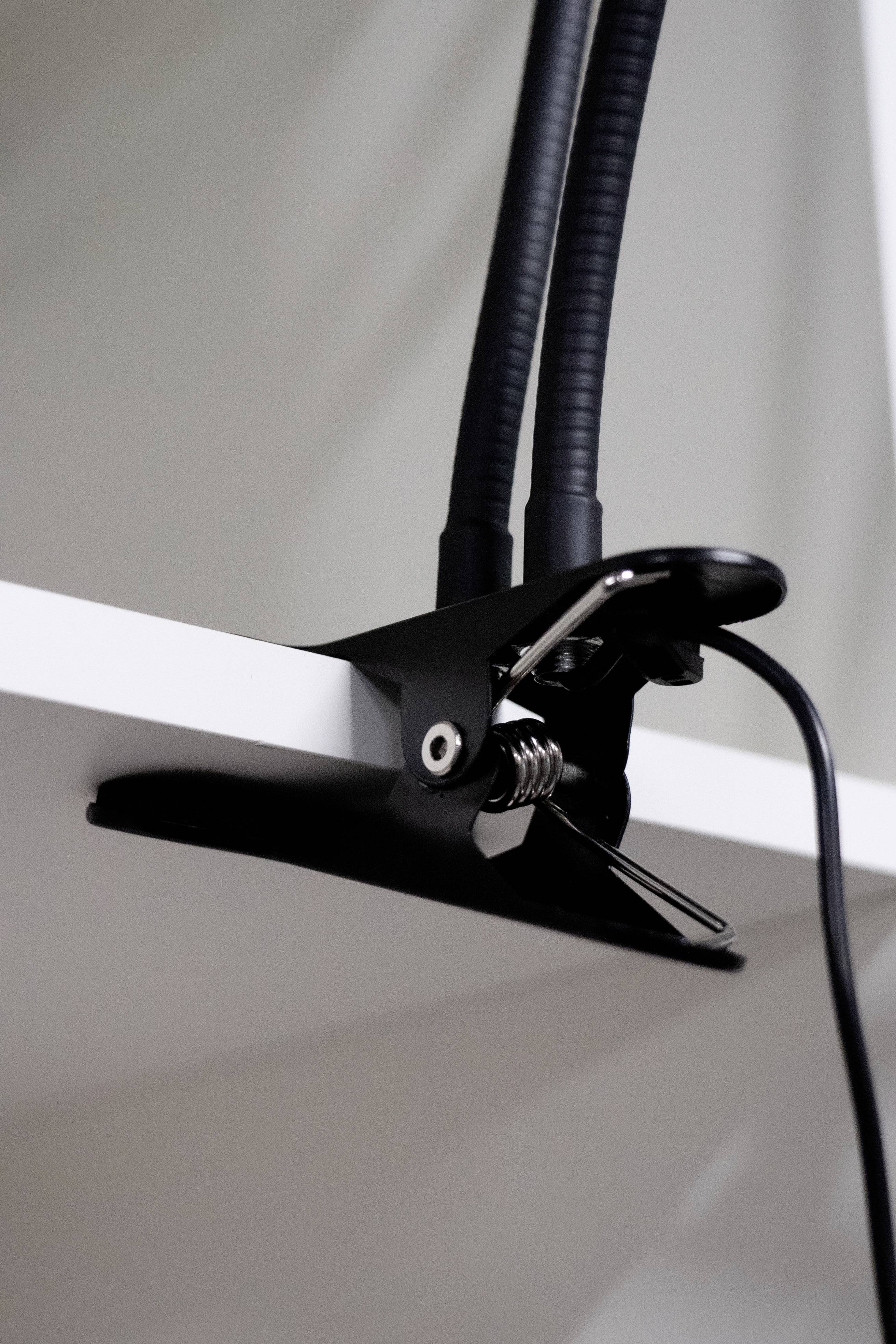A black clip holds a lamp to the edge of a white table. A cable hangs down from the clip.