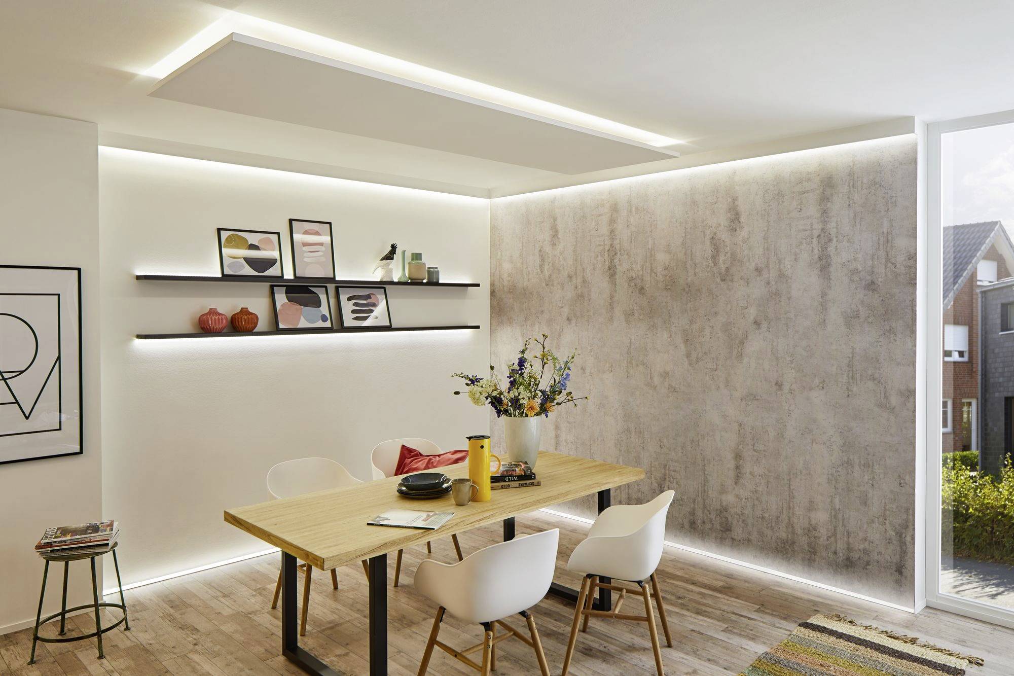 Dining room with a wooden table, four white chairs and modern lighting. Decorative shelves with art and vases on the wall.
