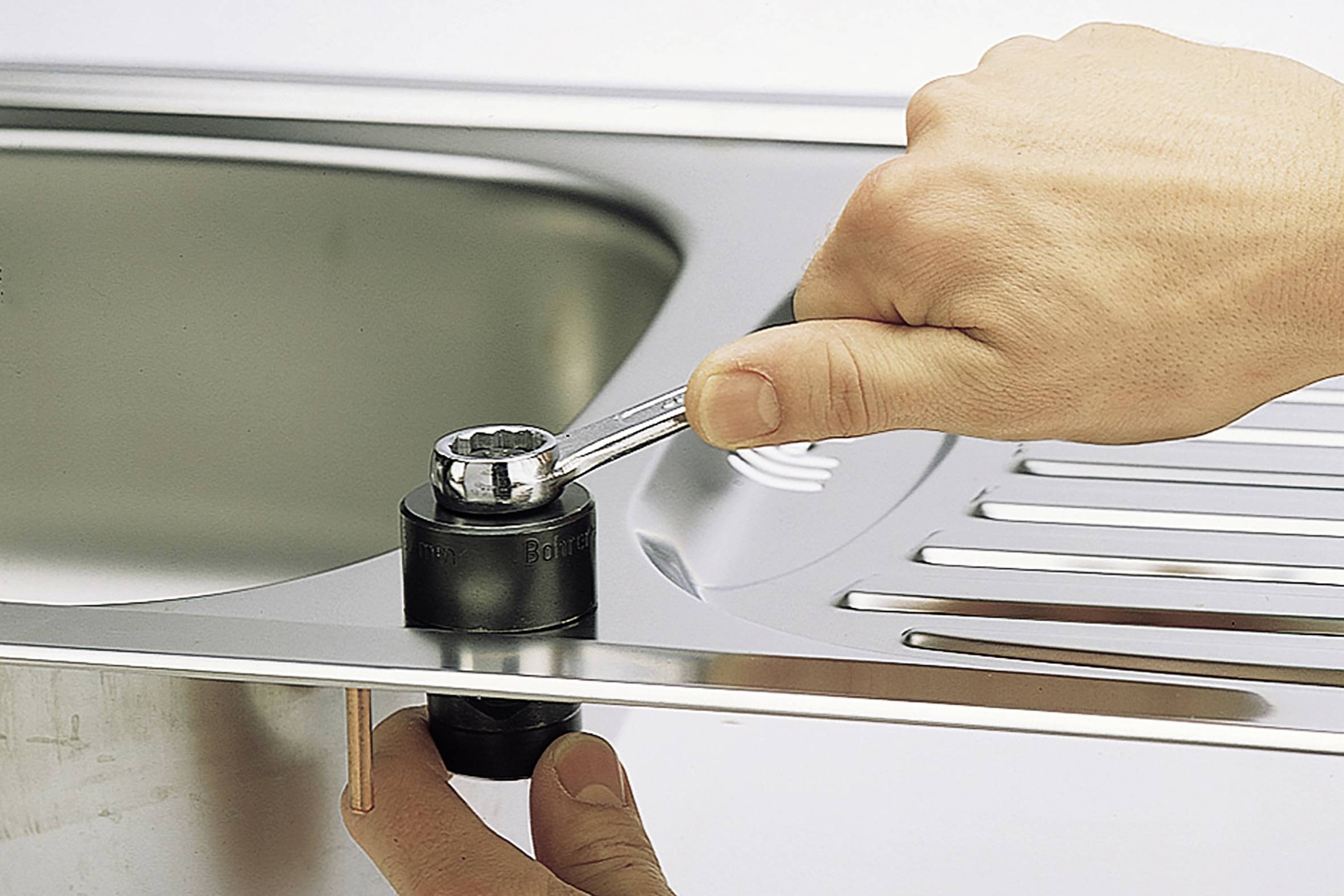 A hand uses a spanner on a fitting beneath a kitchen sink.