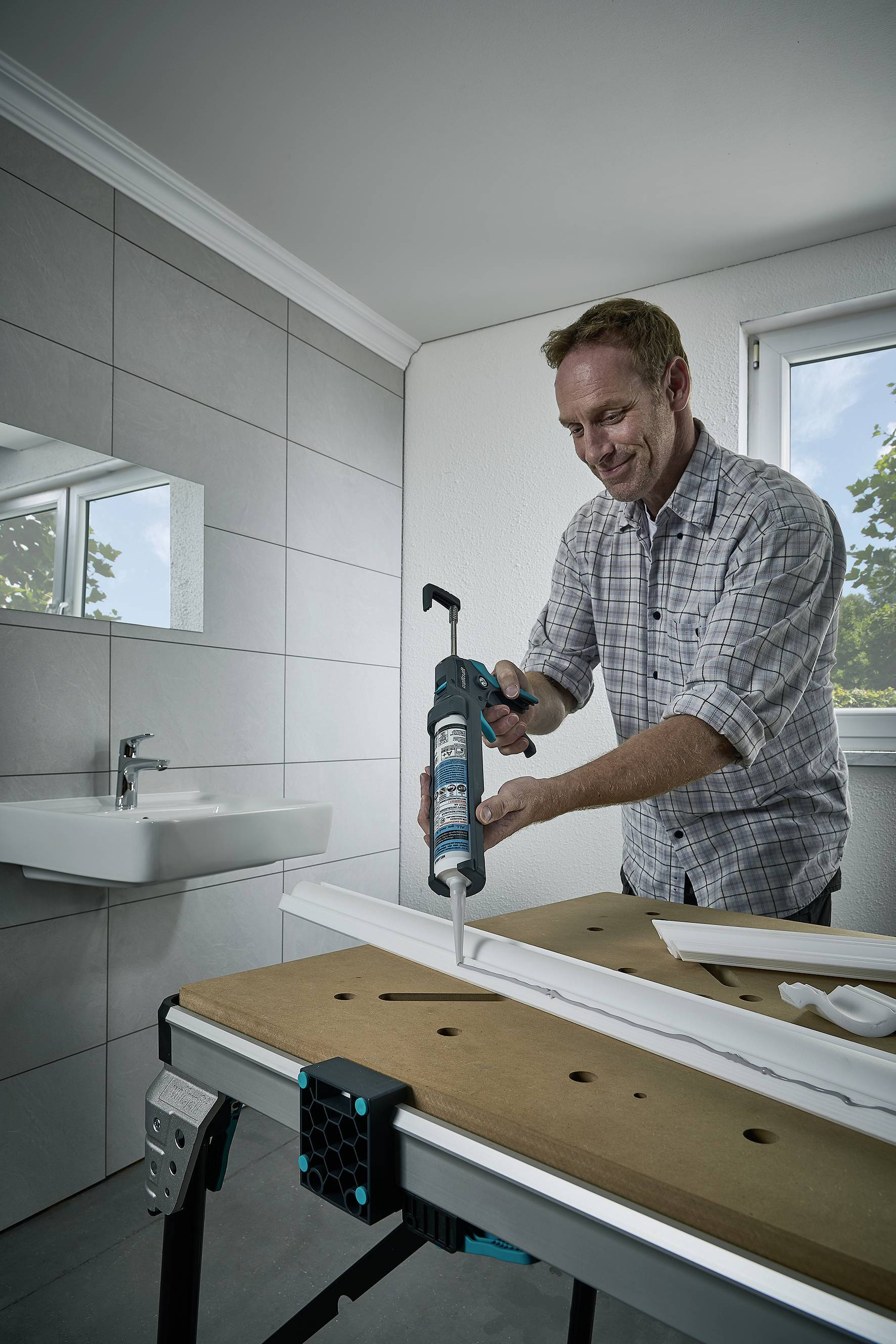 A man is using a caulking gun to apply sealant to a surface. A bathroom can be seen in the background.
