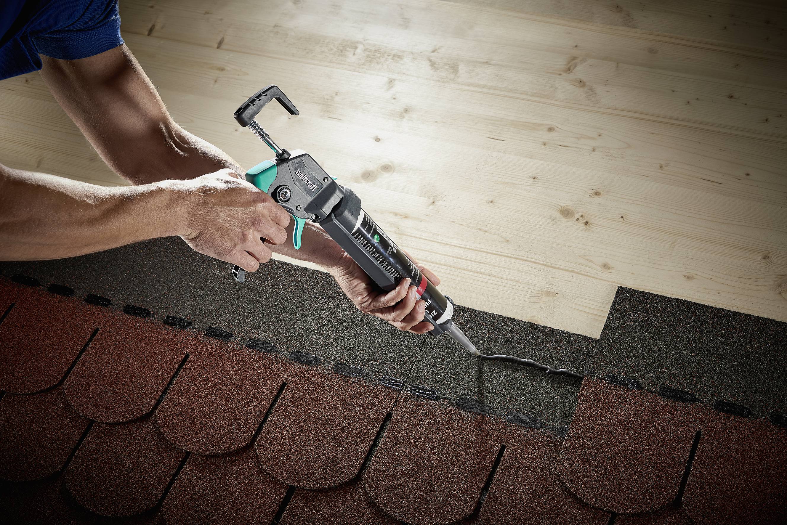 A person is using a cartridge press to secure roof tiles on a roof. The roof is composed of red and grey tiles.