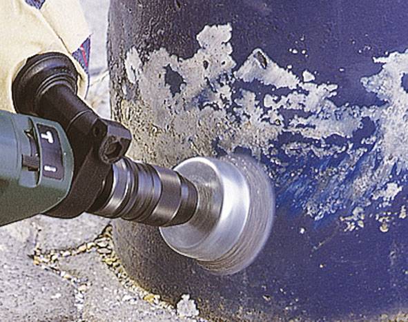 An angle grinder is used to remove paint from a metal cylinder. The grinding disc rotates rapidly across the surface.