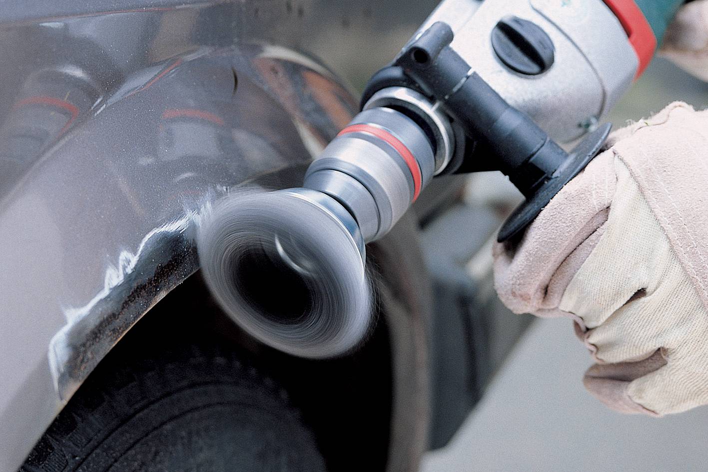 A person is polishing a car door with an electric polishing machine to remove scratches. Hands are wearing gloves.