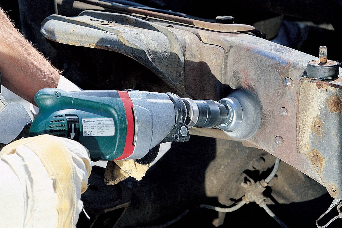 A person is grinding rust off a metal frame, likely on a vehicle, using an electric grinding machine.