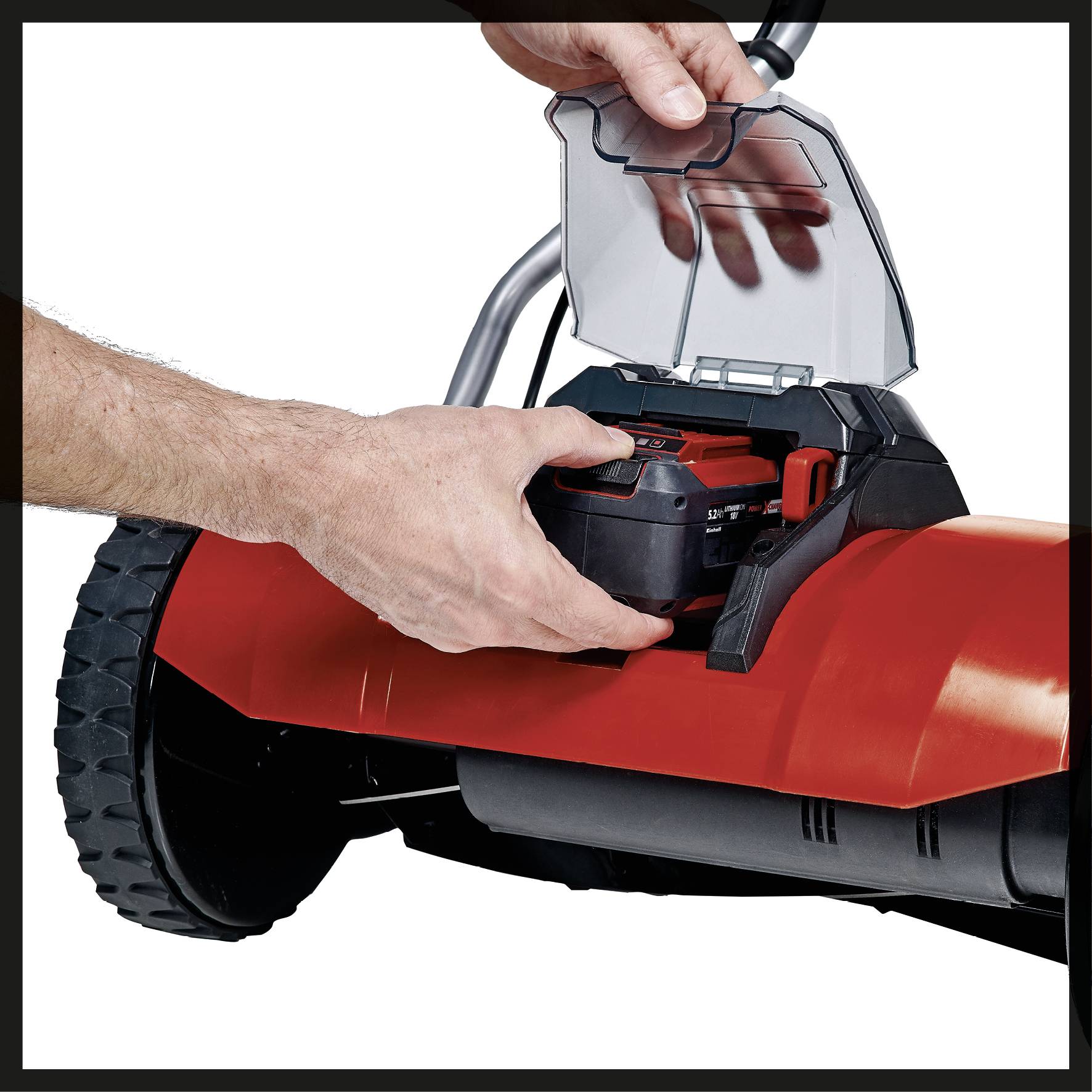 A person is inserting a battery into a red, electric garden tool. The device has large wheels and is likely a lawnmower.