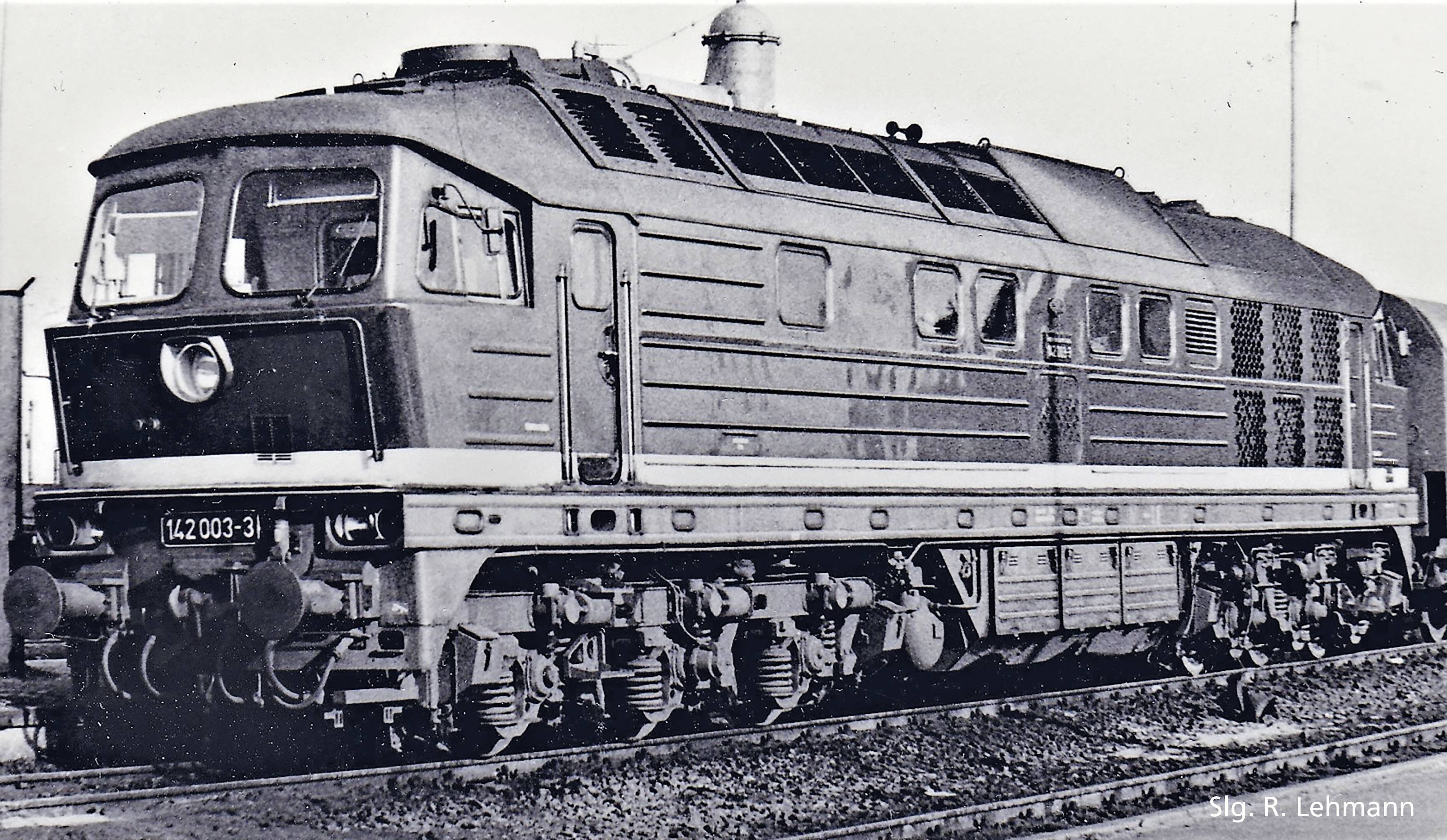 An older railway locomotive on a track. The black and white image shows the side and front view of the vehicle.