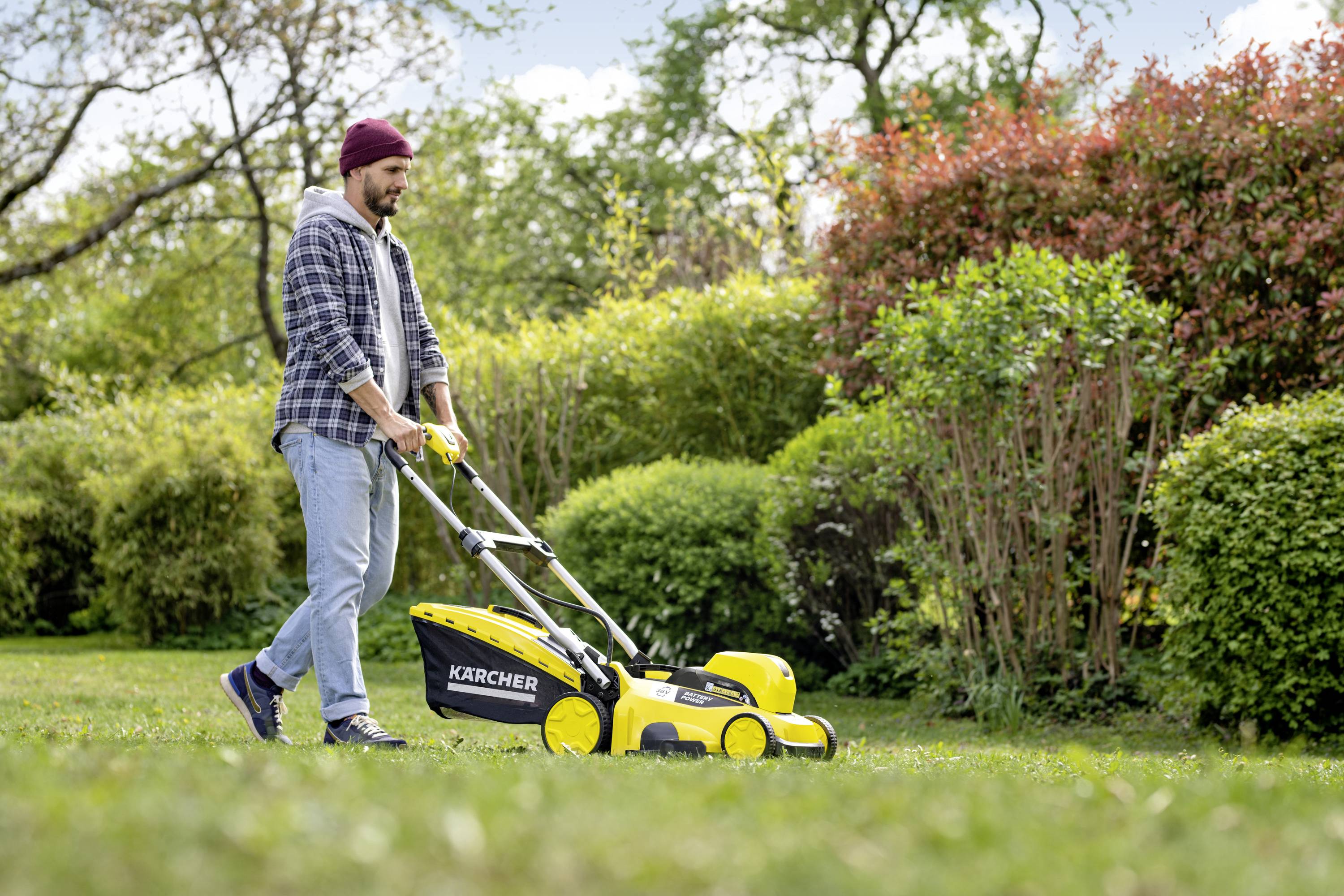 A man is mowing the lawn with a yellow lawnmower in a green garden on a sunny day.