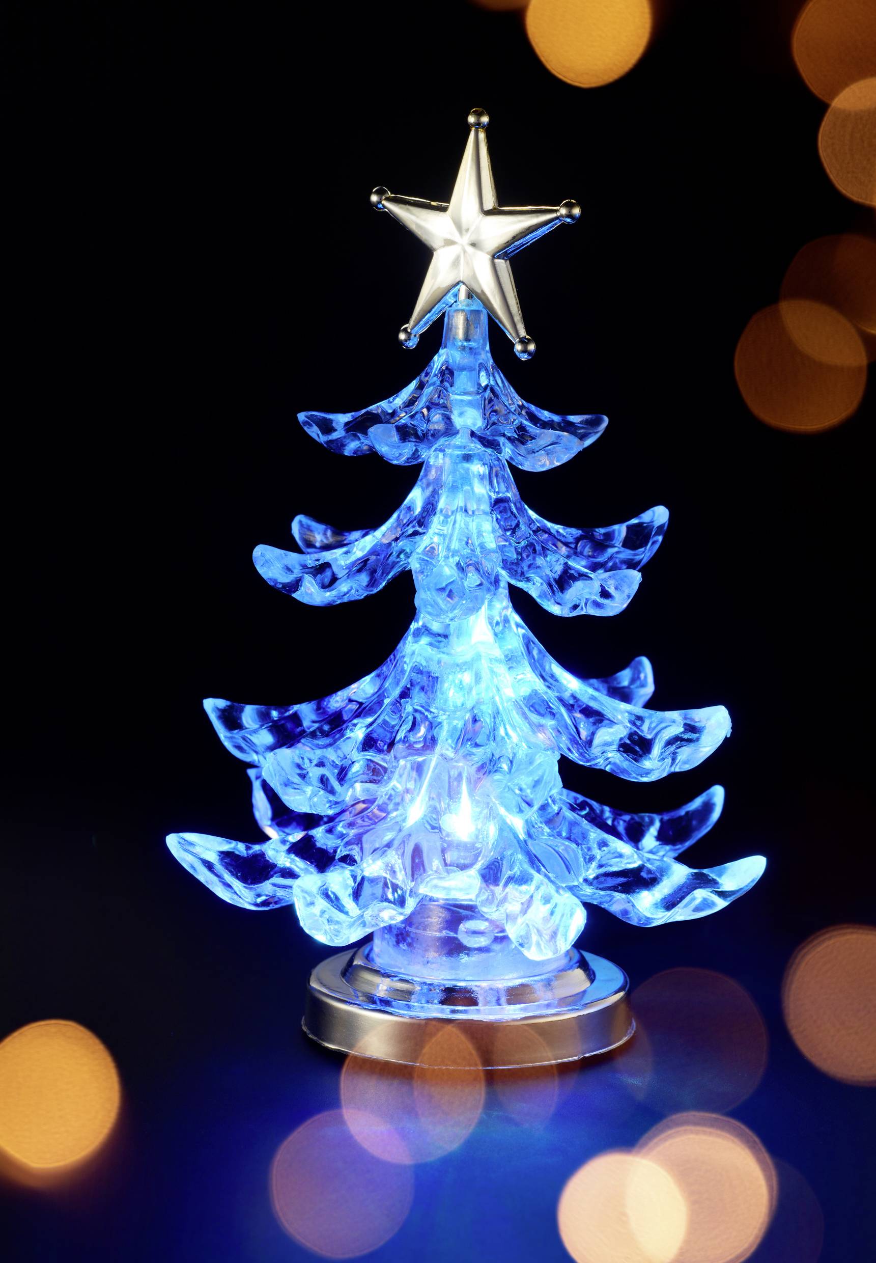 A small, luminous blue Christmas tree with a silver star at its peak. Blurred lights can be seen in the background.