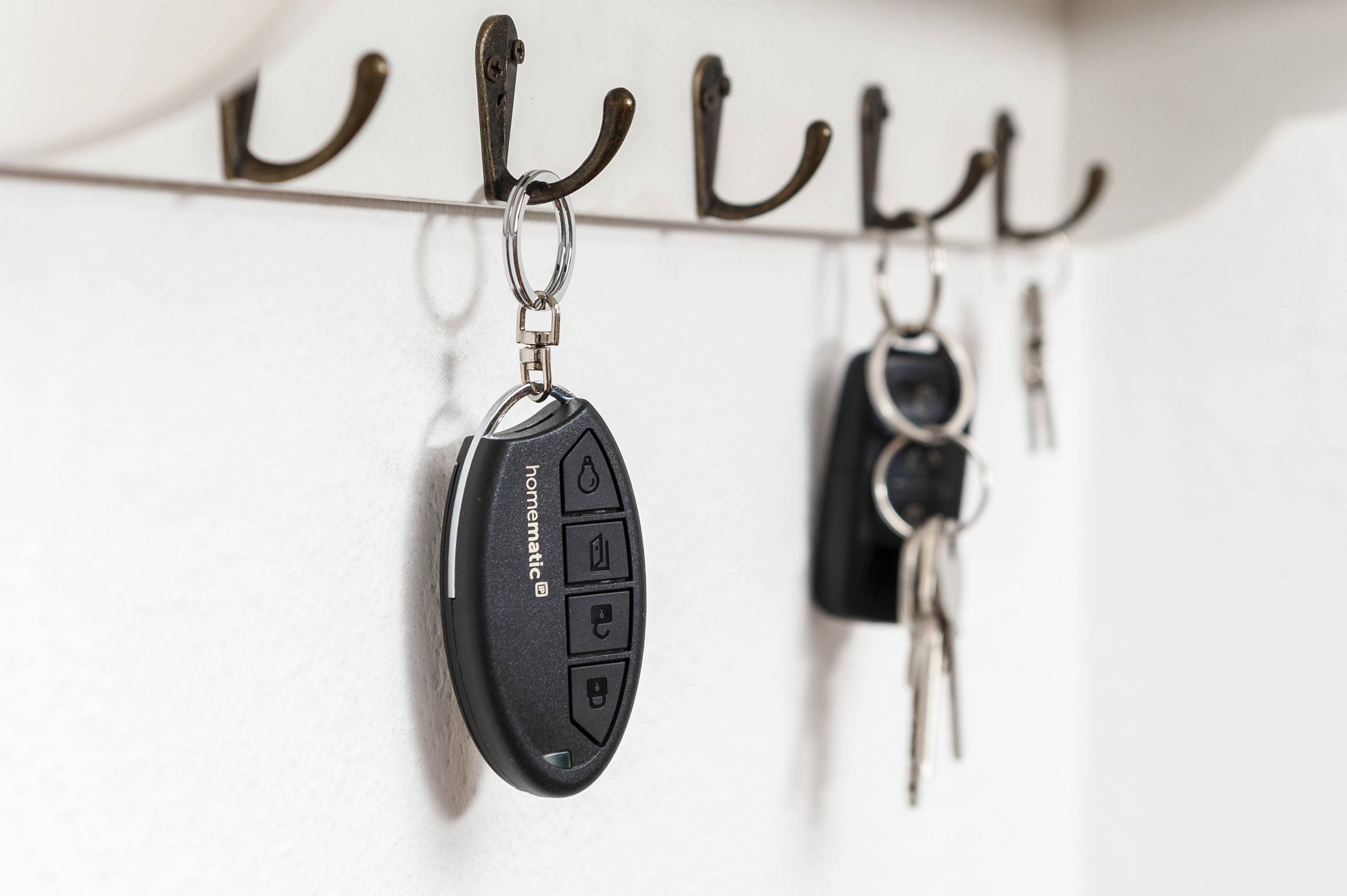 A bunch of keys with a remote control hanging on a wall hook rail.