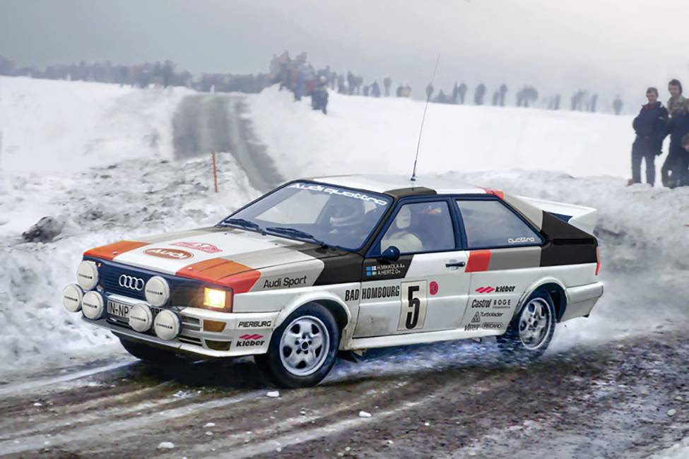 A rally car speeds along a snow-covered route. Spectators are standing by the roadside. The car bears the number 5.