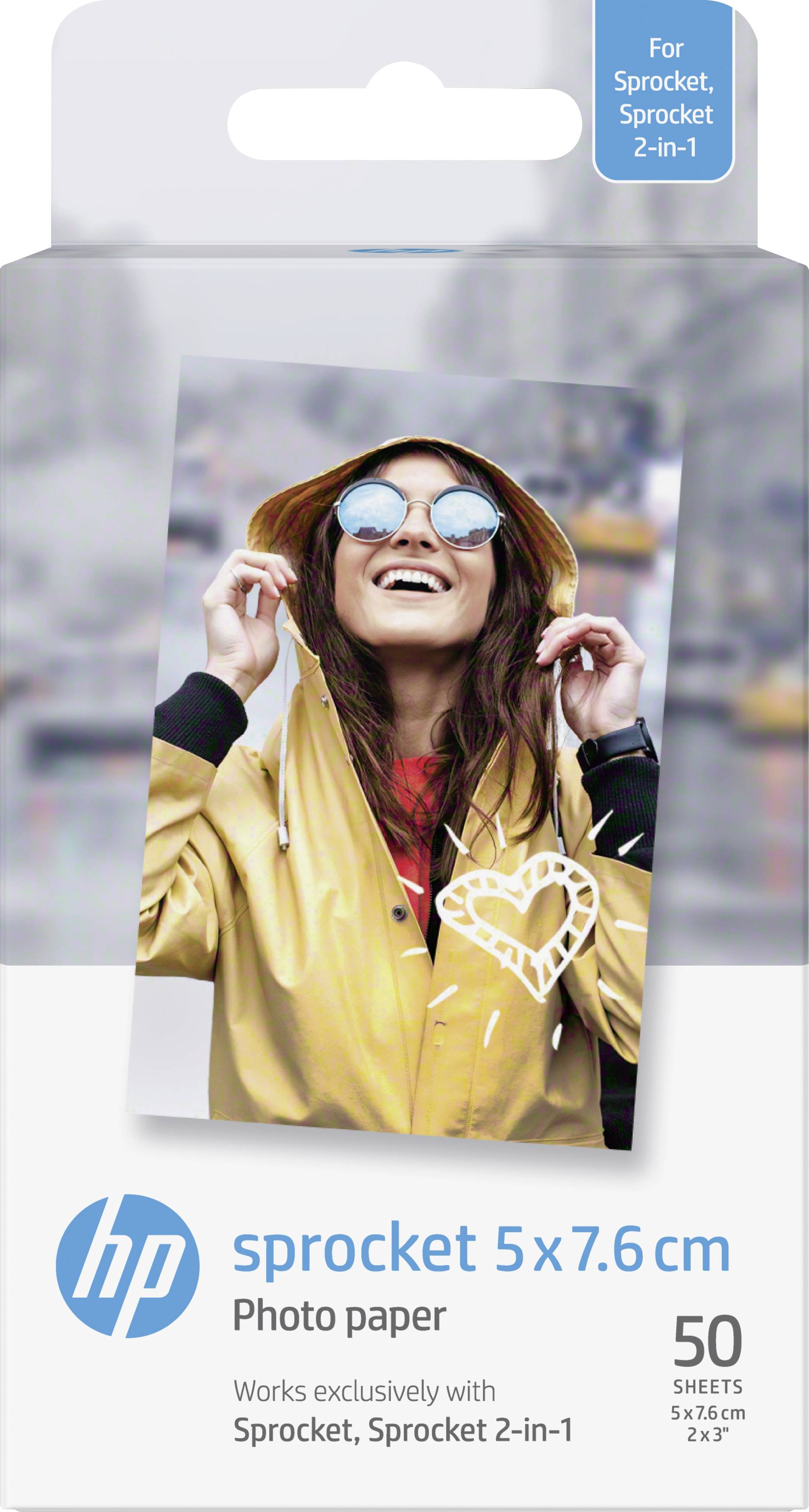 Young woman in a yellow jacket and sunglasses smiles and holds hood in an urban setting. Packaging for HP Sprocket photo paper.