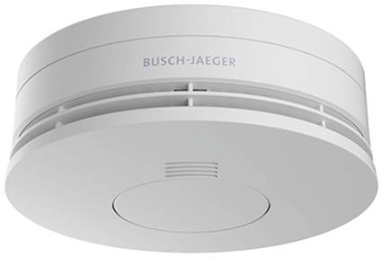 Smoke detector in close-up. The round, white detector shows several ventilation slots and bears the inscription 'Busch-Jaeger'.