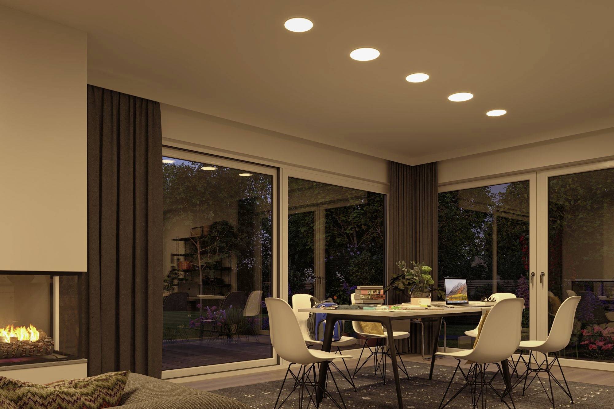 Cosy living room with a dining table and white chairs, fireplace lit and garden view through large windows.