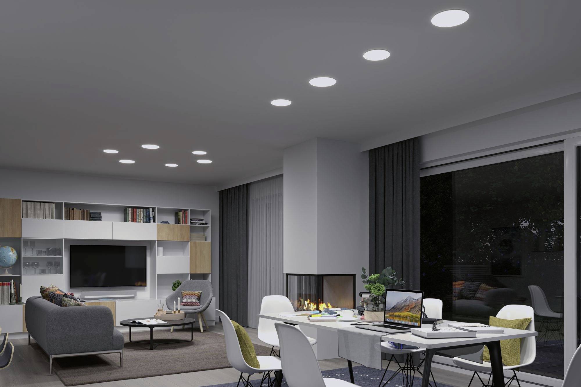 Open-plan living room with modern furnishings: sofa, built-in fireplace, dining table with laptops and chairs; multiple ceiling lights.