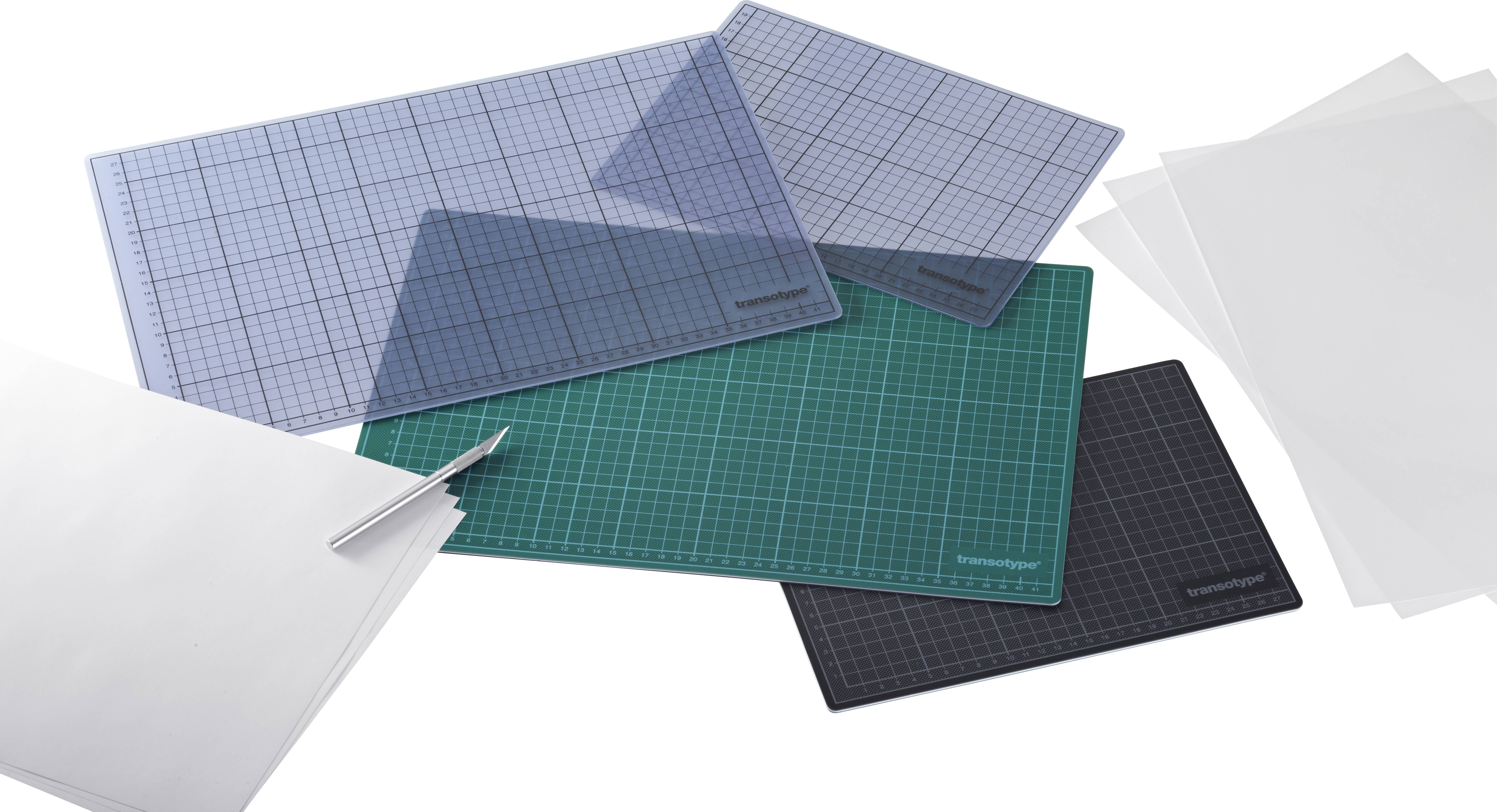 Various cutting mats in blue, green and black on a table, with white sheets of paper and a pen lying beside them.