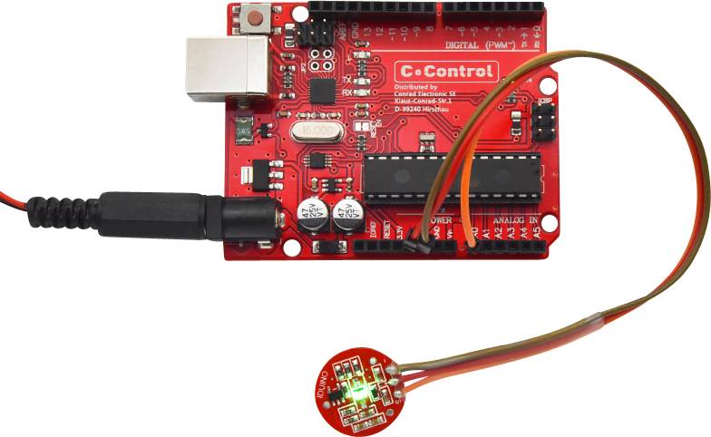 Arduino-like board with microcontroller and LED; red circuit board with connectors and cables, LED glowing green.