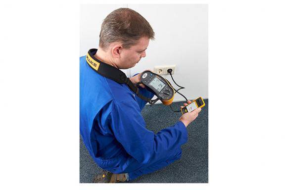 A technician in blue workwear is measuring the voltage at a socket using two devices.