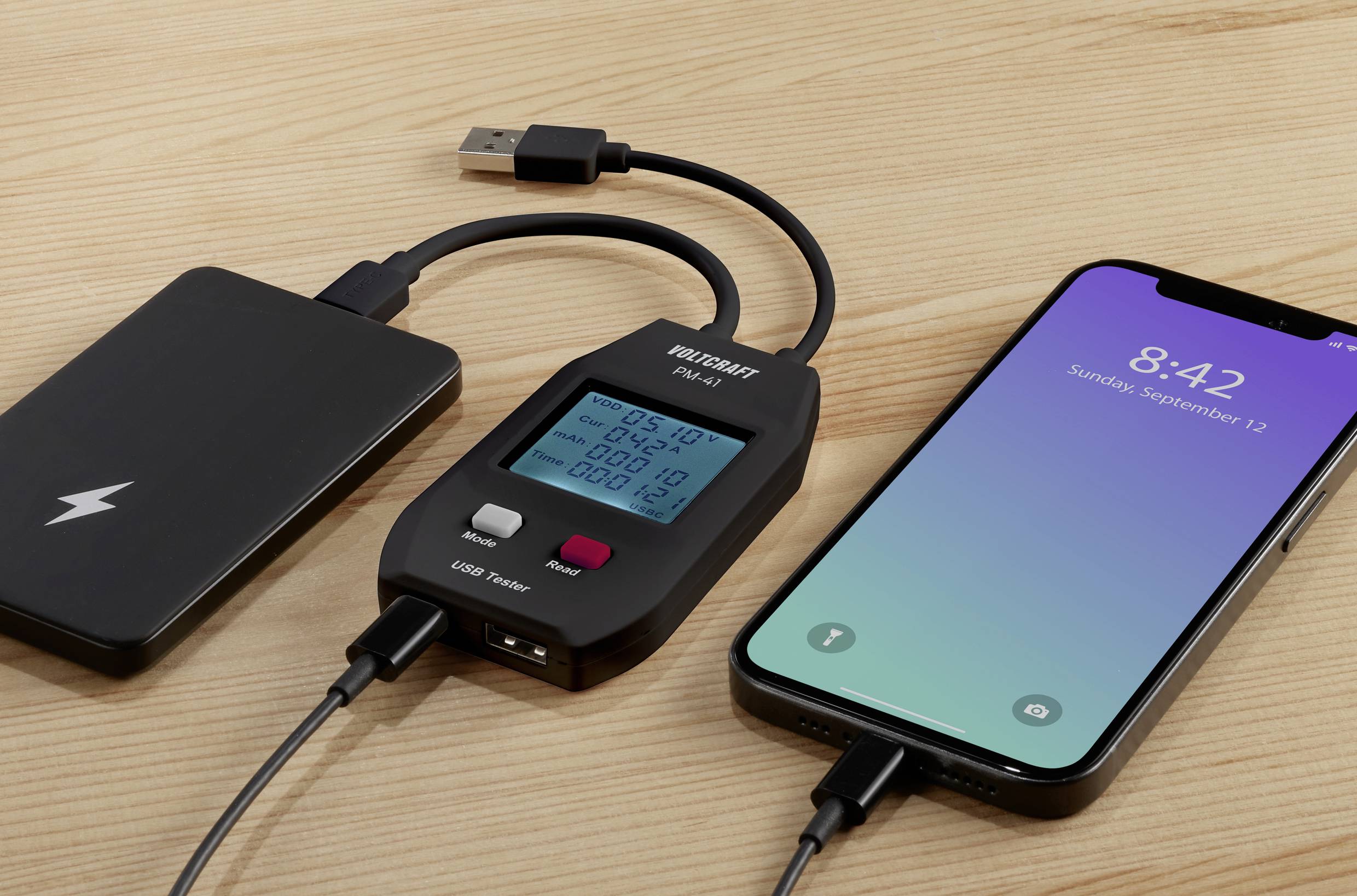 A smartphone displays the time '8:42' and is connected to a USB power meter, which is in turn plugged into a power bank.
