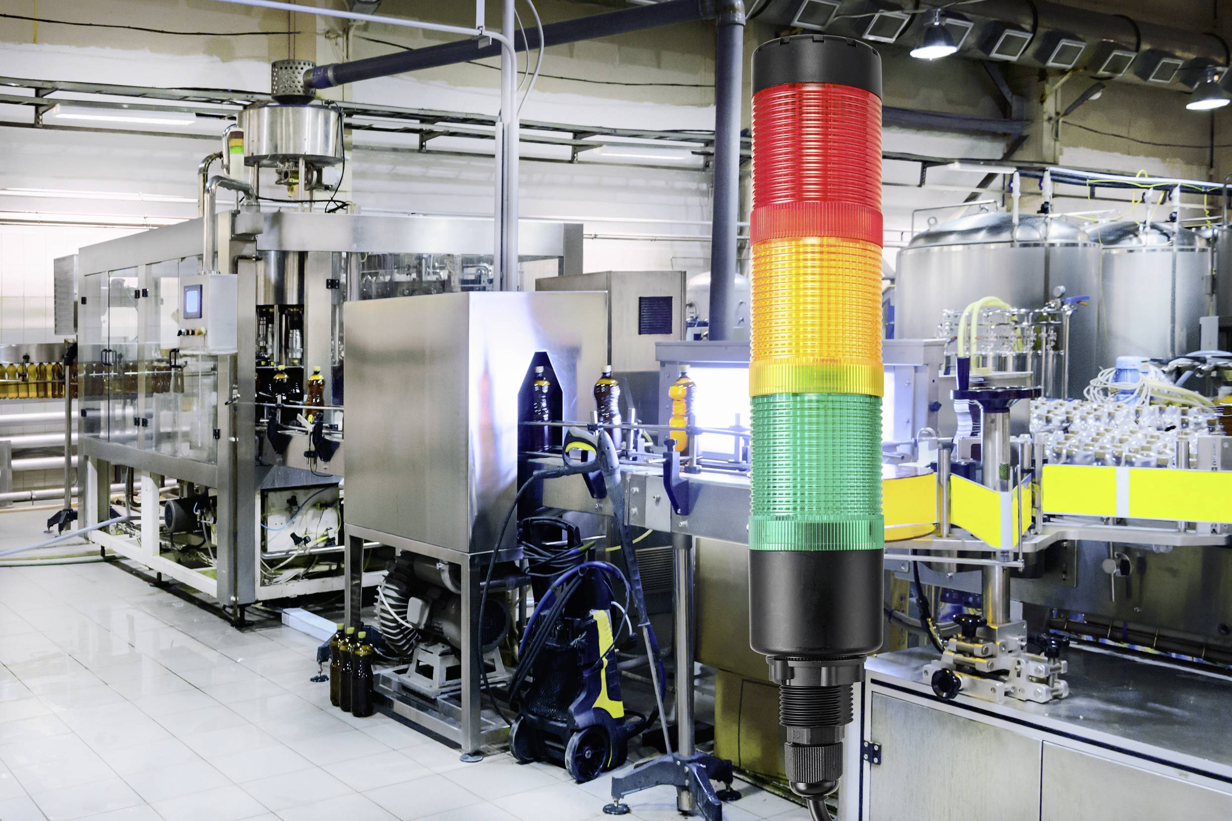 Conveyor belt in a factory with modern machinery in the background; in the foreground, a multi-coloured signal LED display indicating operational status.
