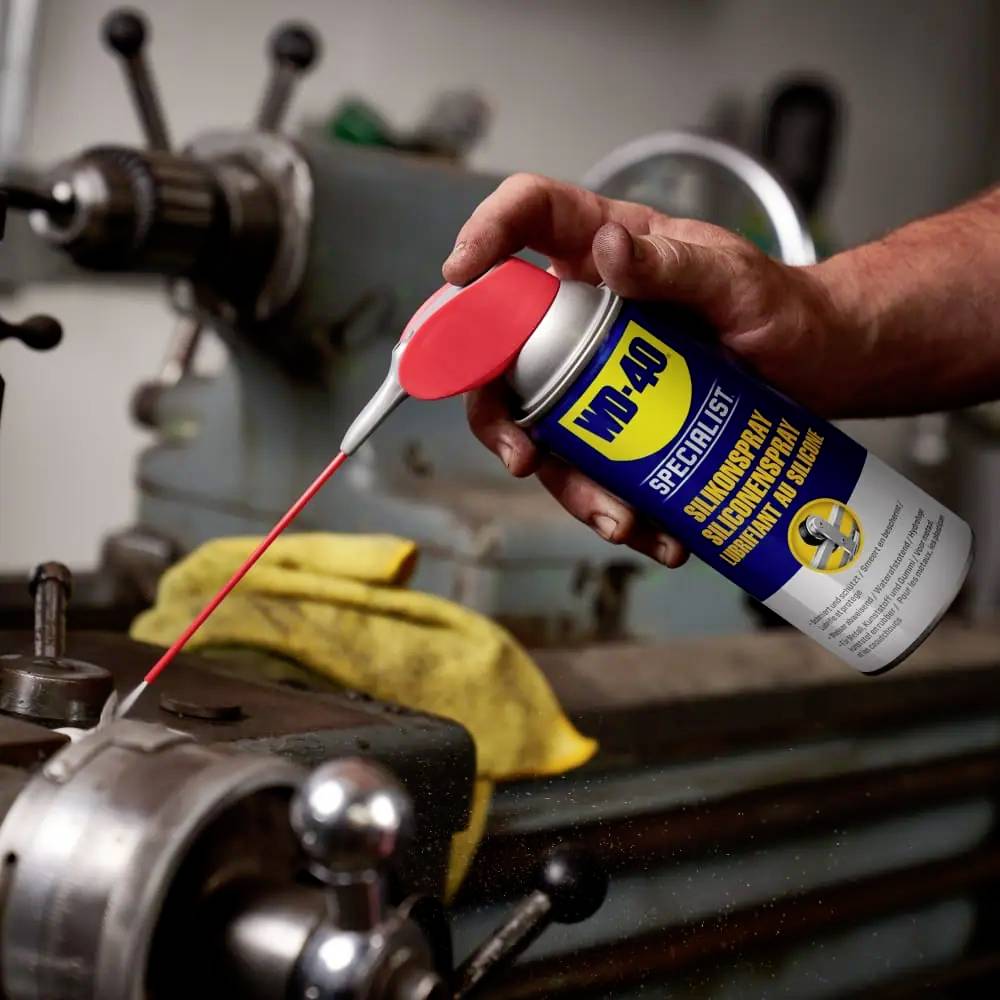A person sprays lubricant from a WD-40 can onto the moving part of an old lathe to maintain it.