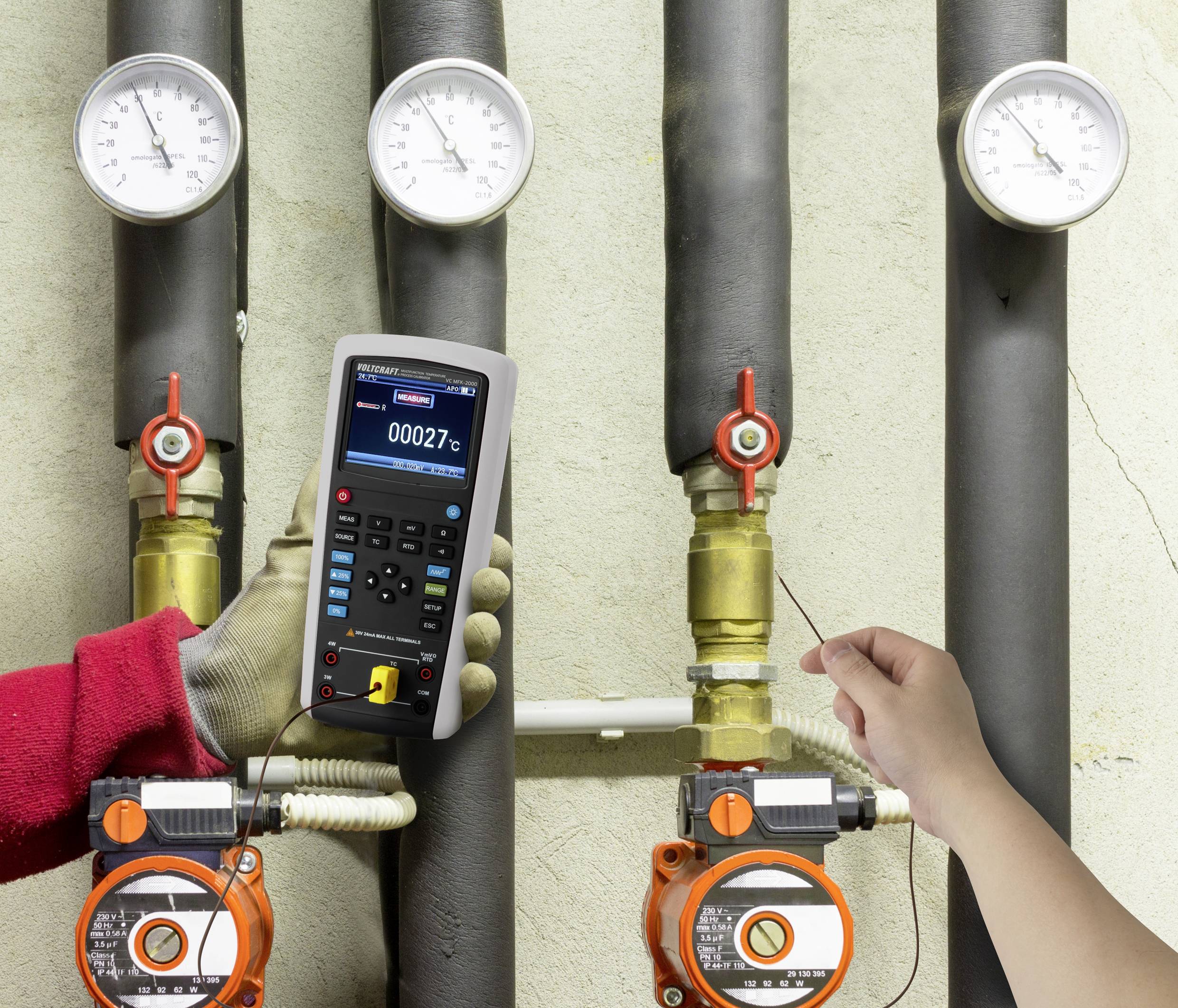 A technician is checking pipe temperatures with a digital measuring device, while manual valves are visible beneath the pipework.