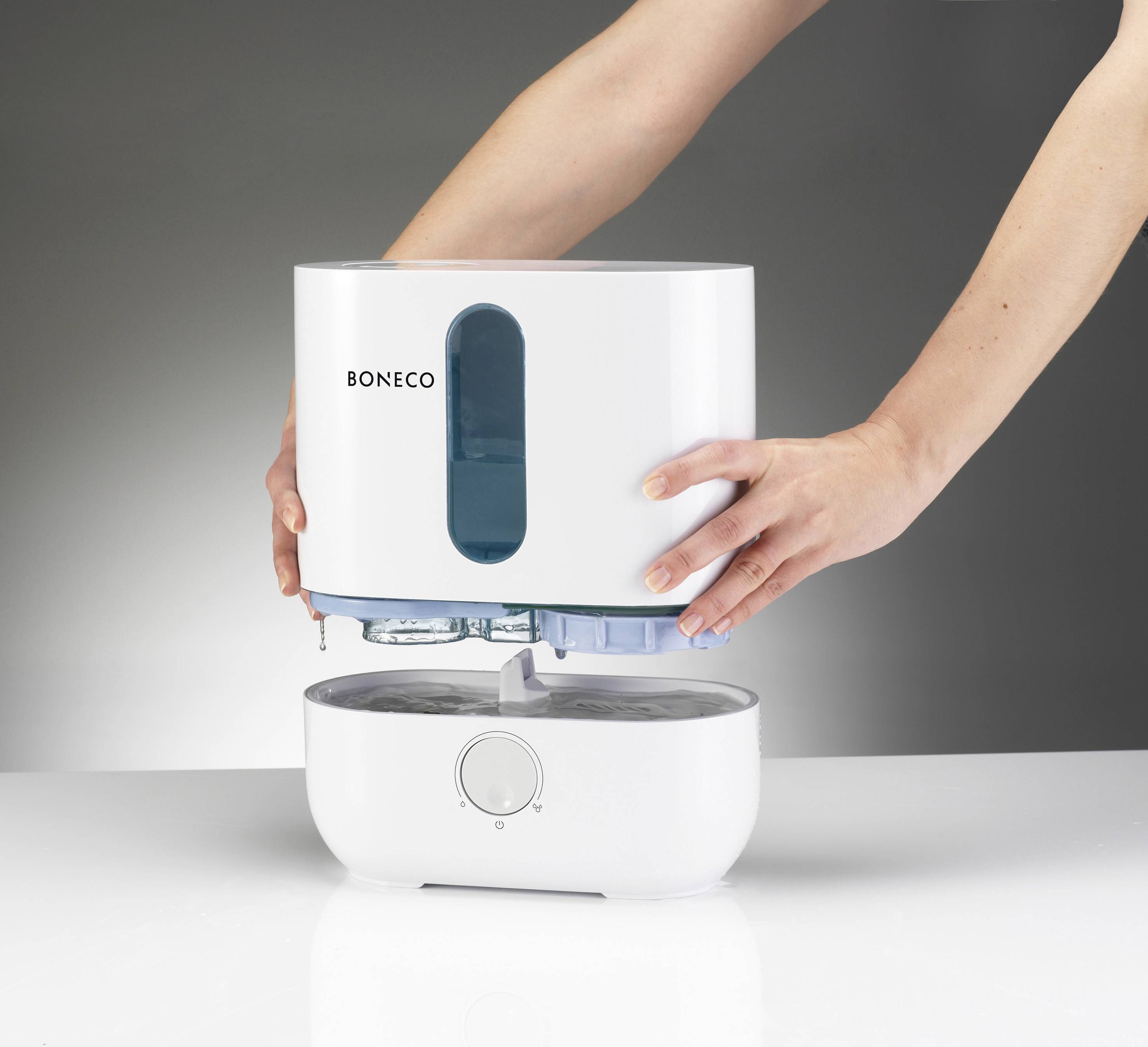 A person is placing the water base of a humidifier onto its assembly. The humidifier is from the Boneco brand.