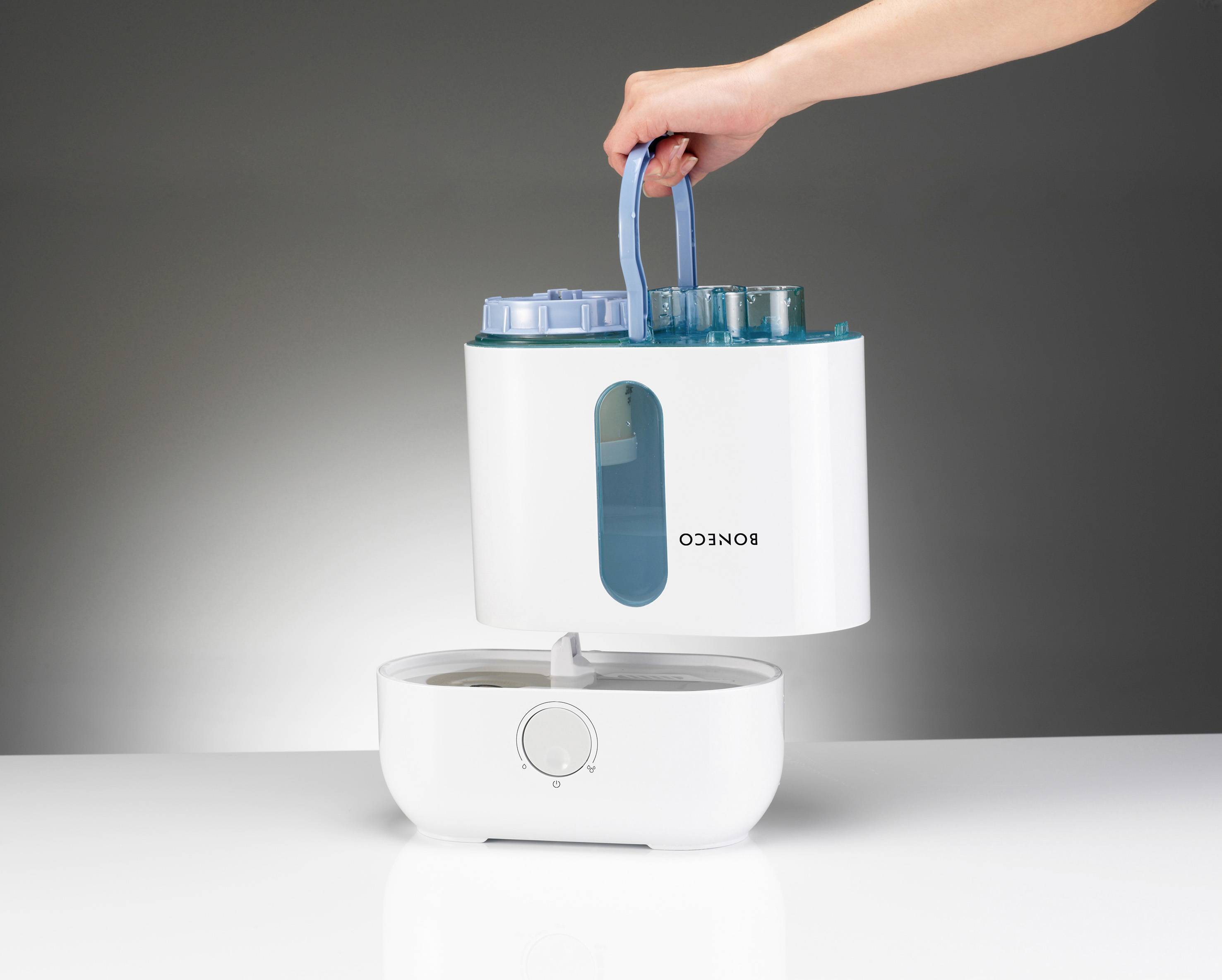 A hand lifts the water tank of a humidifier. The tank is transparent blue and is being pulled out from the top.