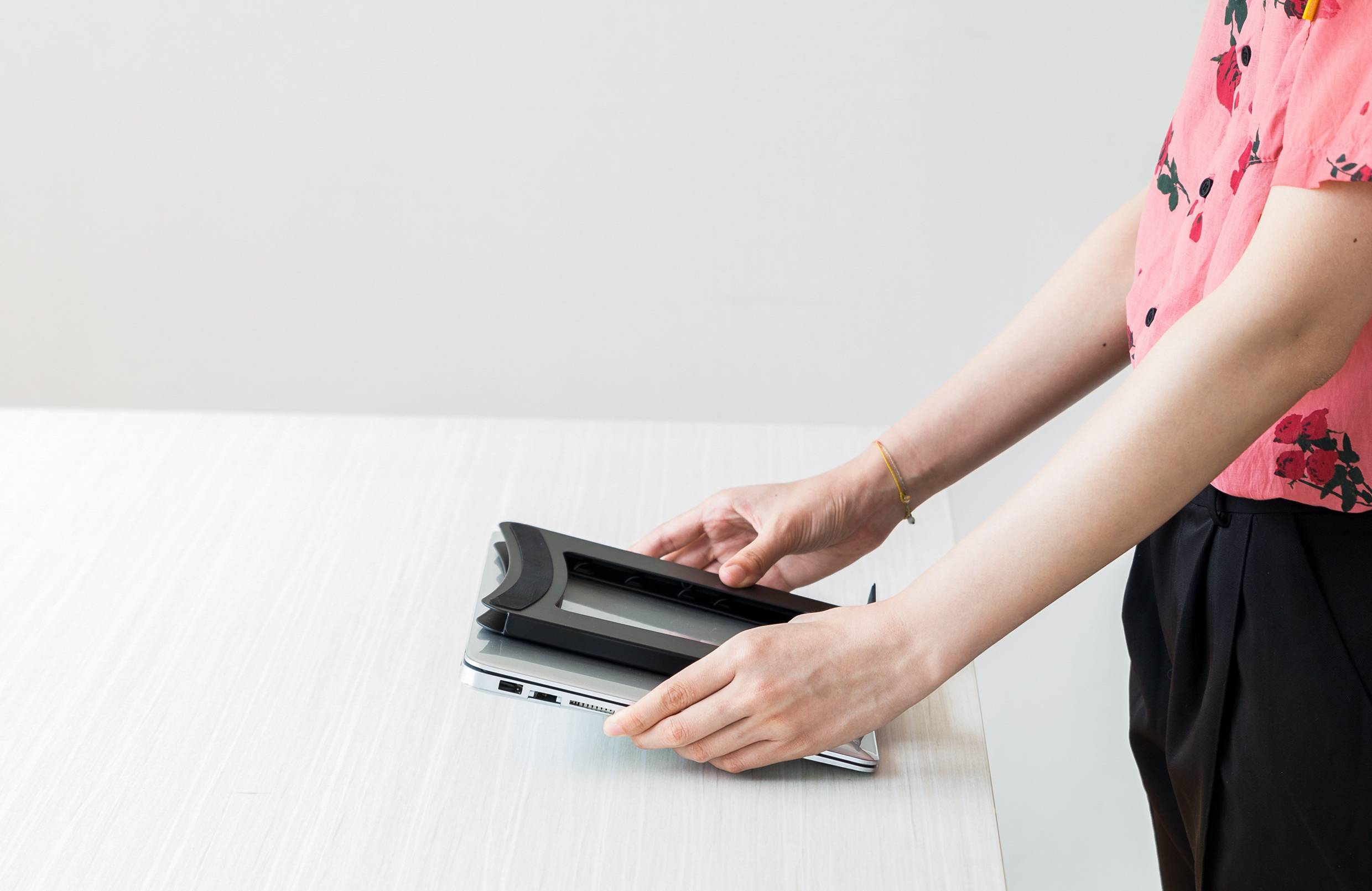 A person in a pink blouse is placing a cover on a closed laptop on a table.
