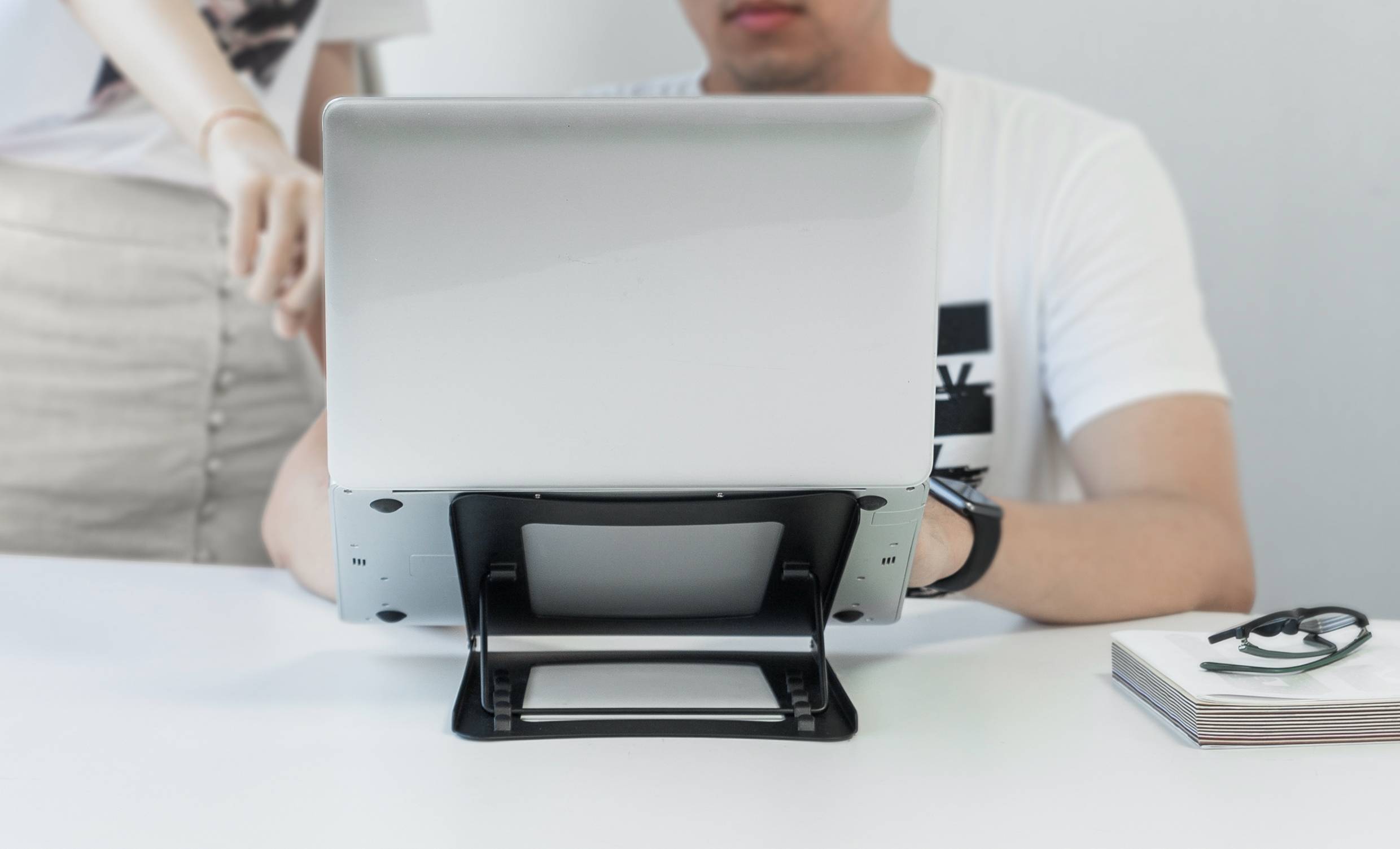 A seated person is working on a laptop, while another person standing is pointing at the screen.