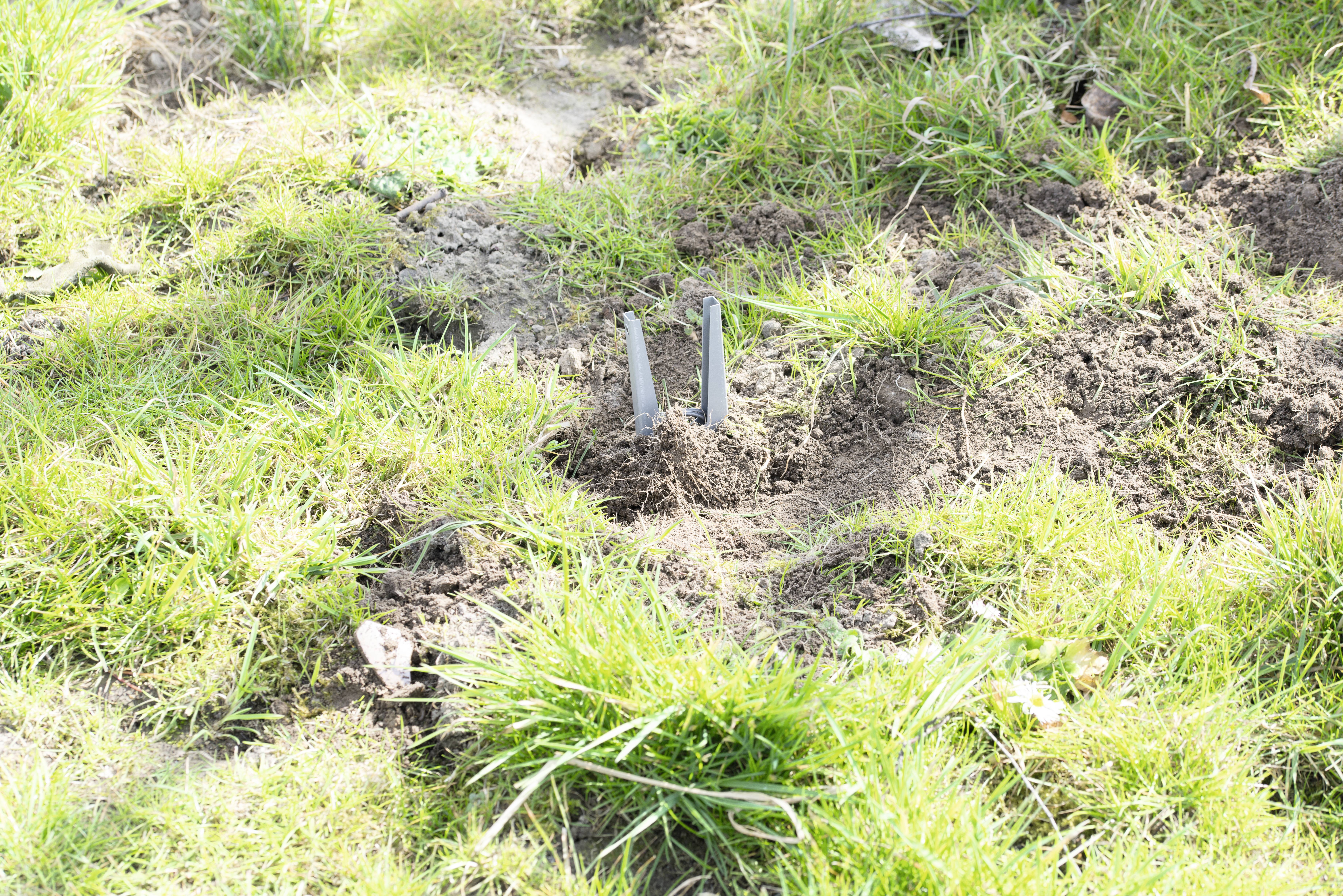 Some metal pieces protrude from the ground in a patch of grass. The surroundings are grassy and slightly unkempt.