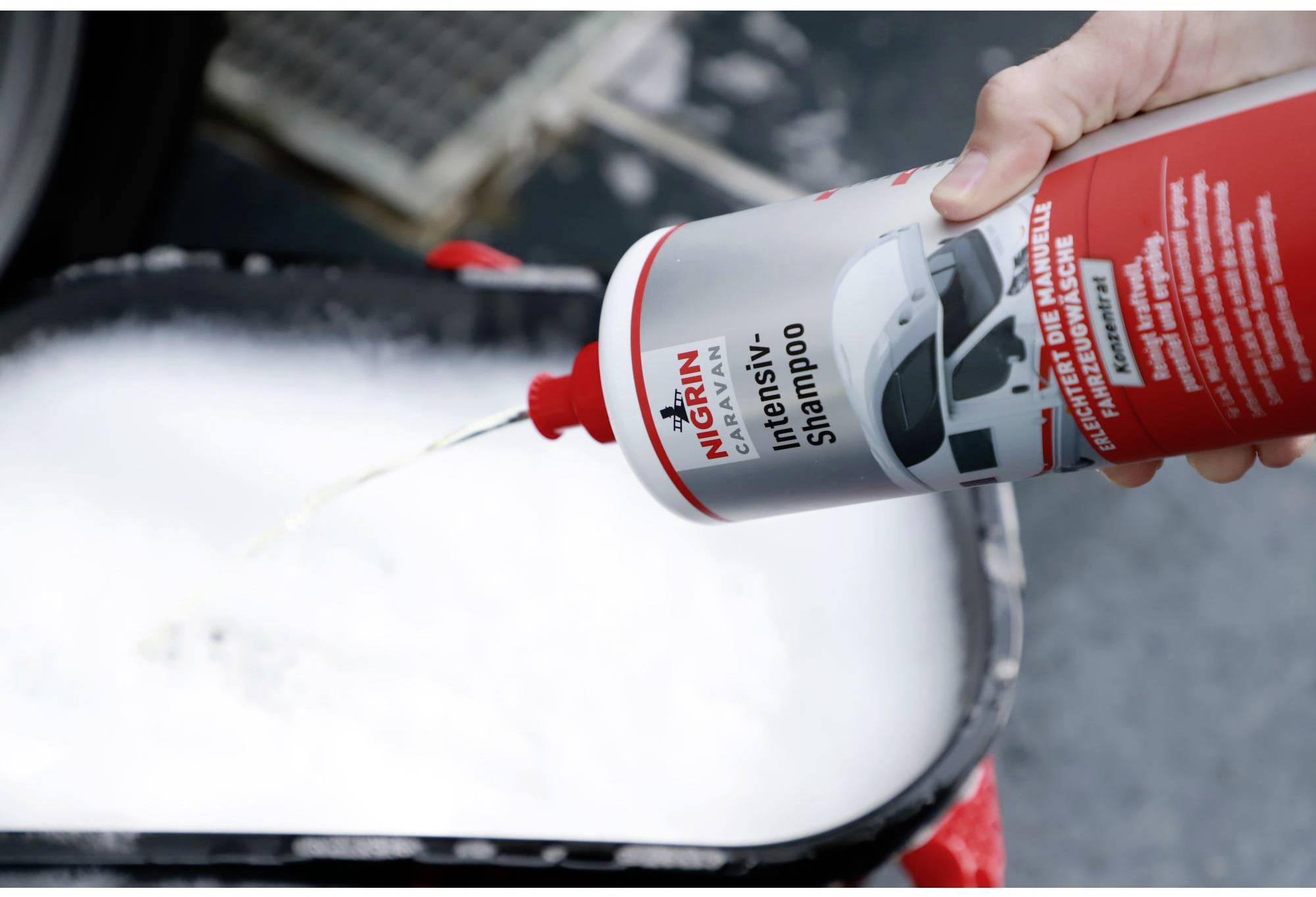 A hand pours NIGRIN Intensive Shampoo into a bucket with foam.